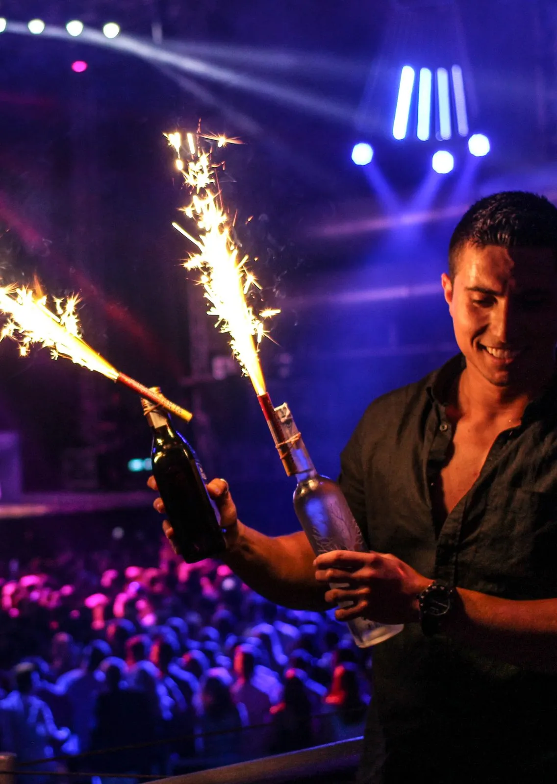 A waiter carrying champagne with sparklers through a club, blue lights sweeping the dance floor, Ibiza