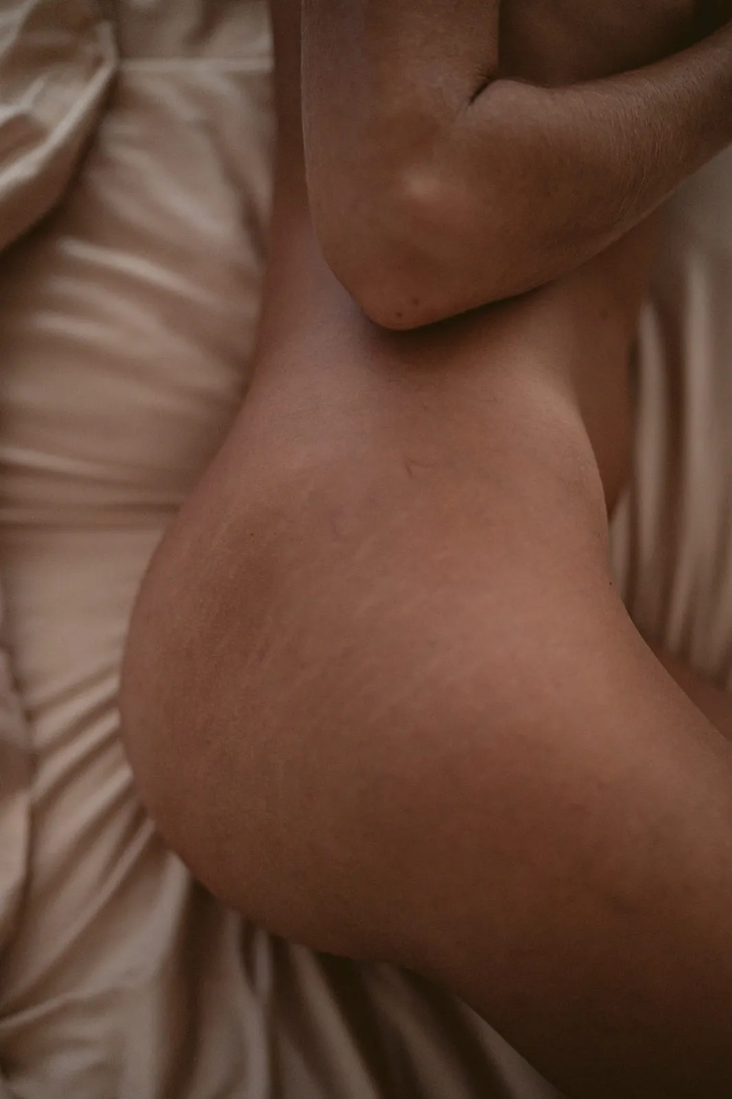 The curve of a bare back and hip against pale linen sheets