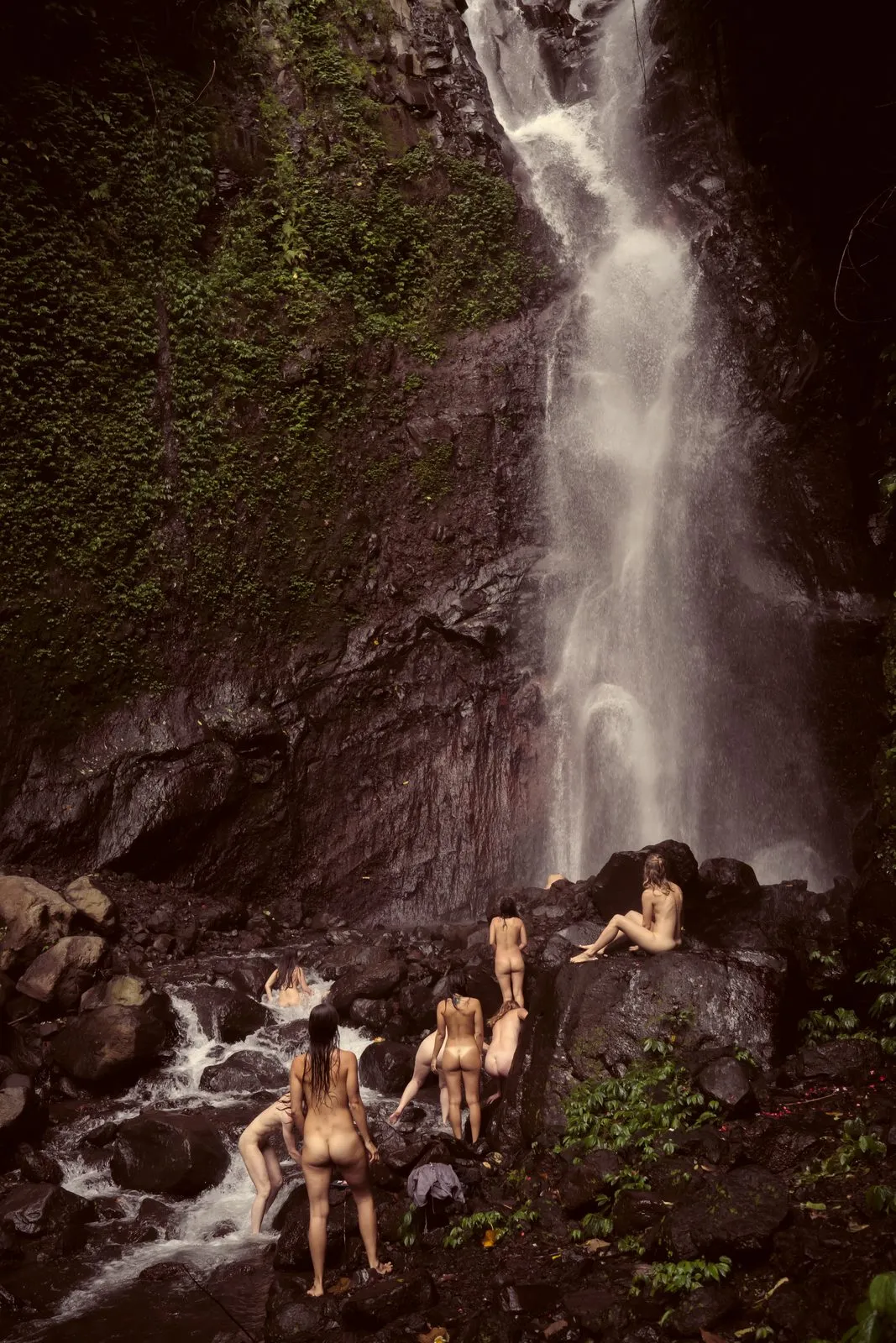 A group of women on the rocks at the foot of a tall waterfall in the rainforest