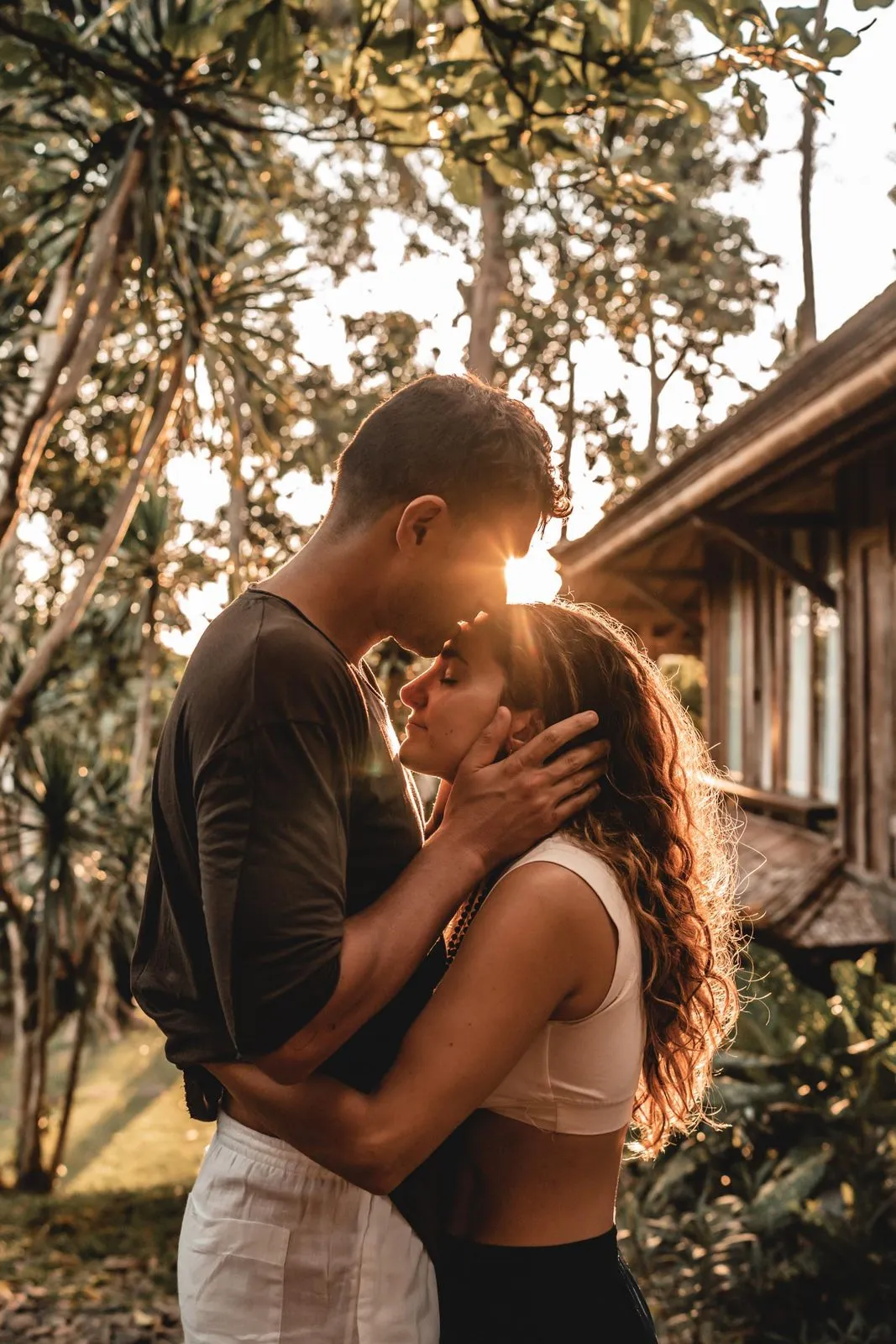 A couple kissing among palms at sunset, the light flaring between them