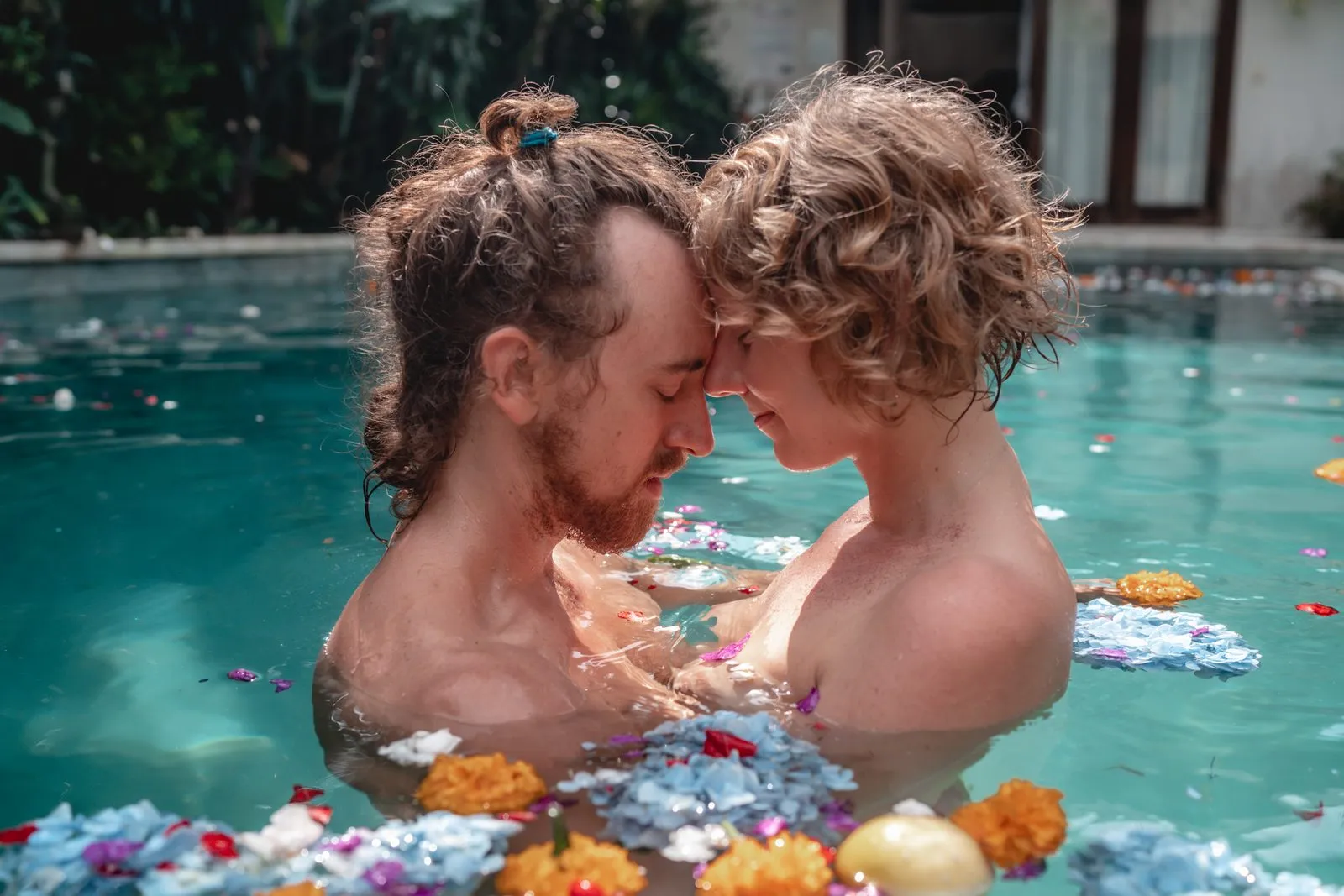 A couple forehead to forehead in a pool scattered with marigolds and petals