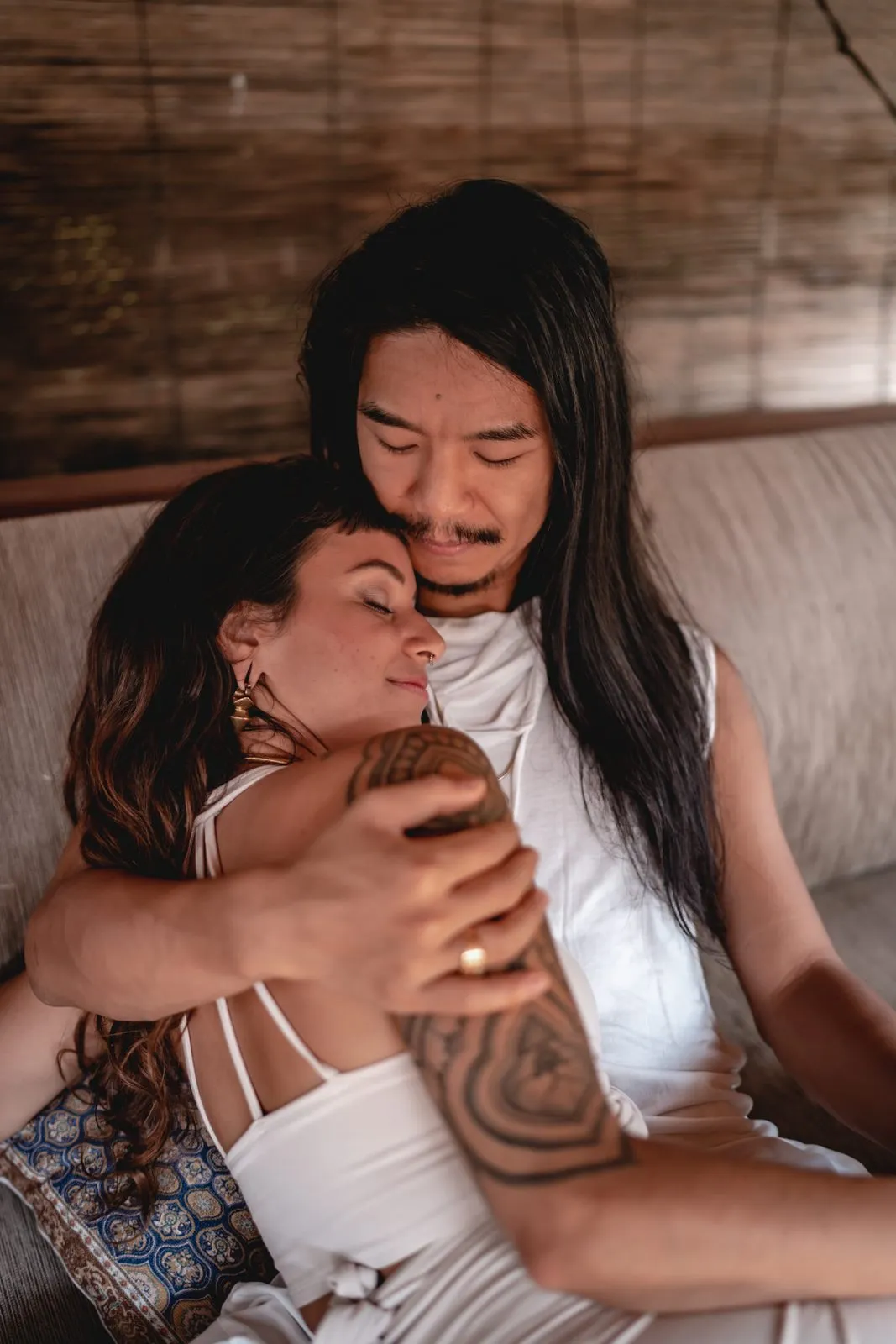 A couple curled together on a sofa, her head against his chest, both in white