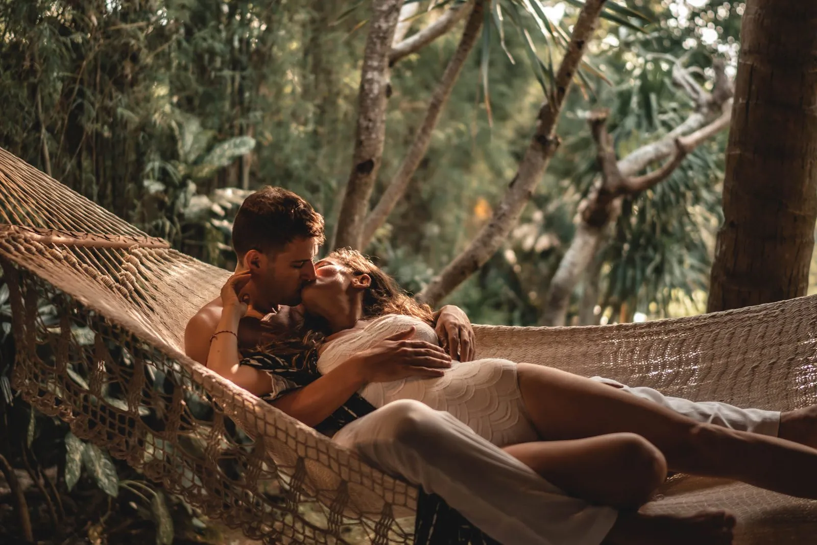A couple lying together in a hammock under the trees, her head on his chest, Bali
