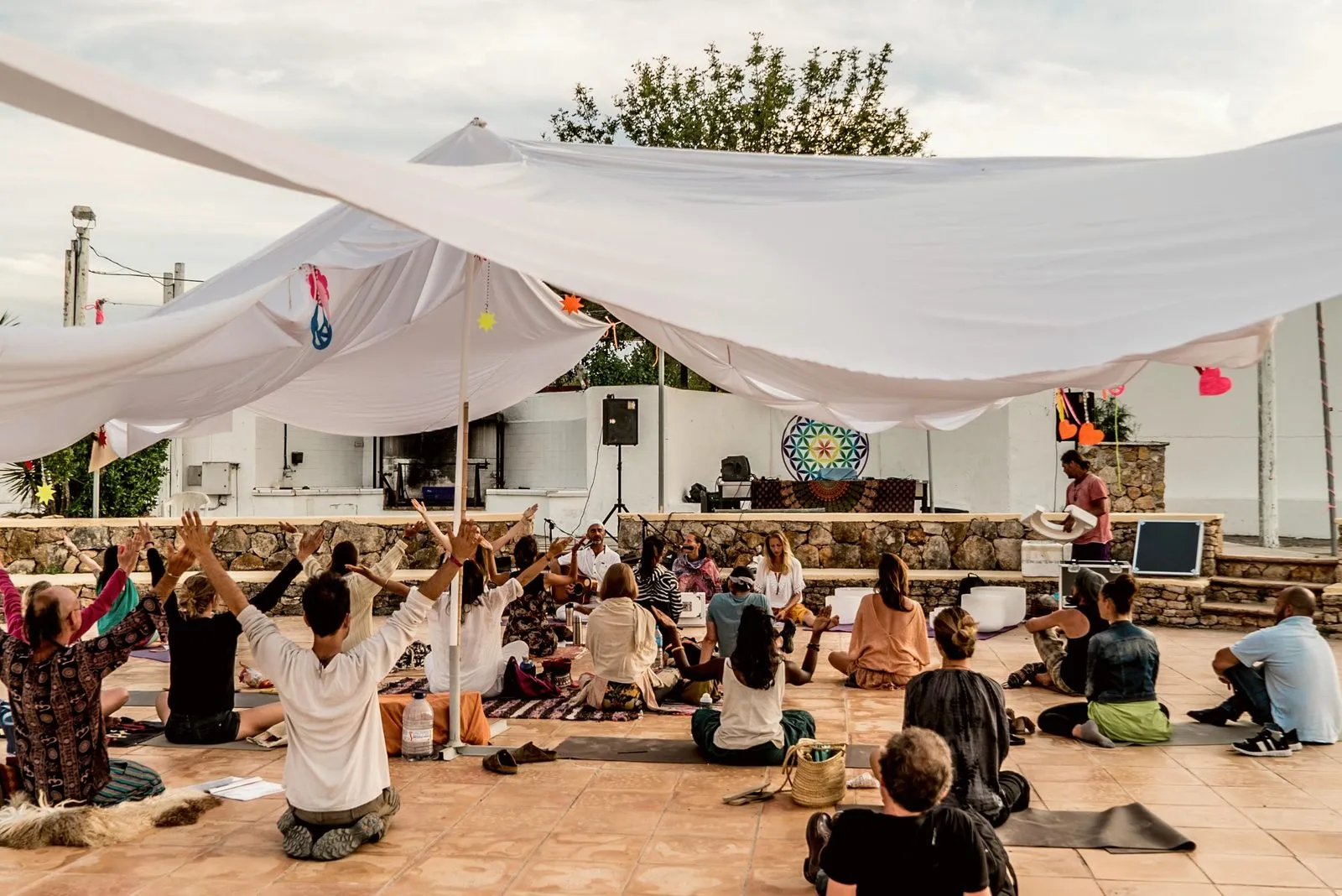 A festival crowd seated under white sail shades, arms raised toward the stage