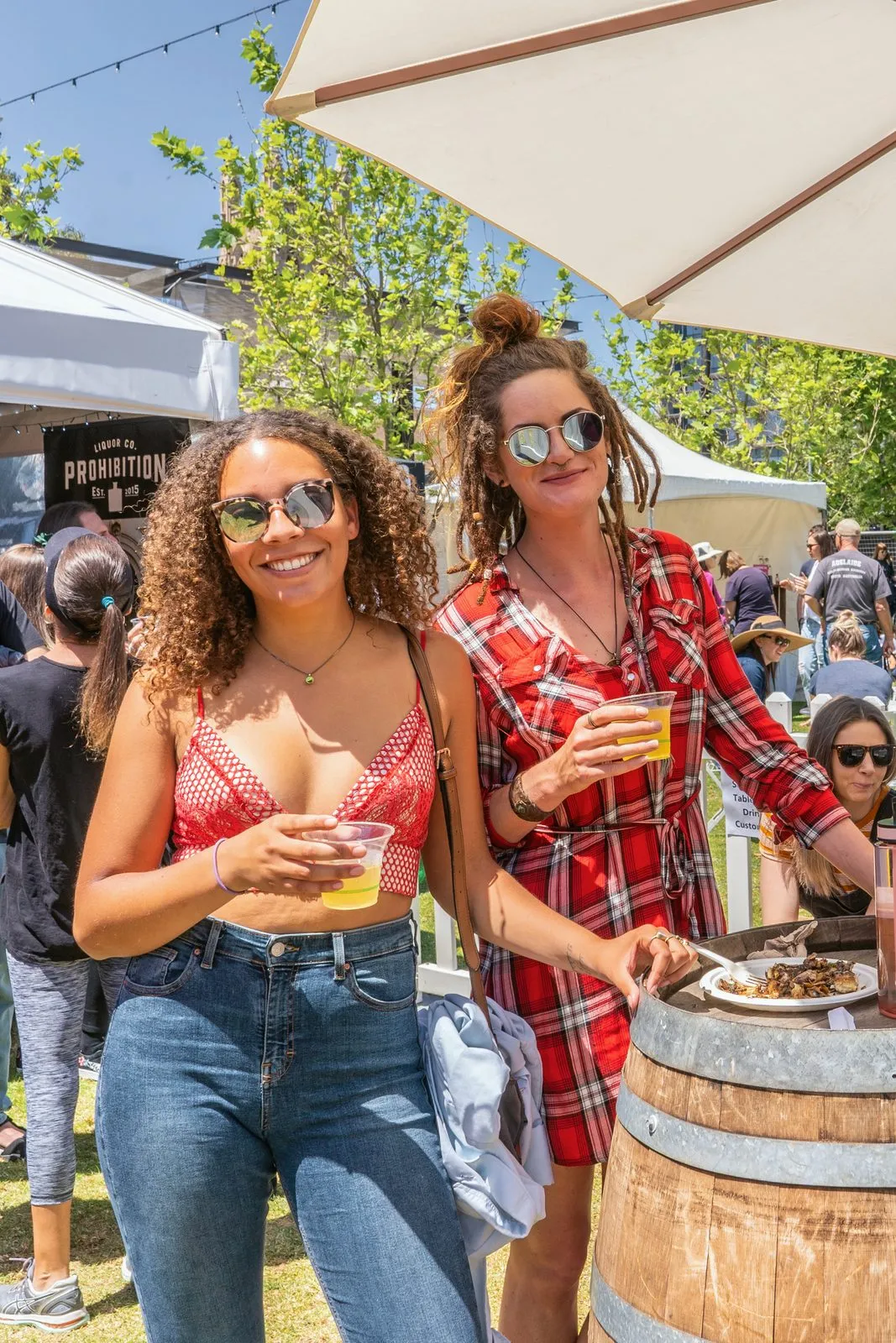 Two friends with drinks under an umbrella at the Adelaide Vegan Festival, one in a red bandana
