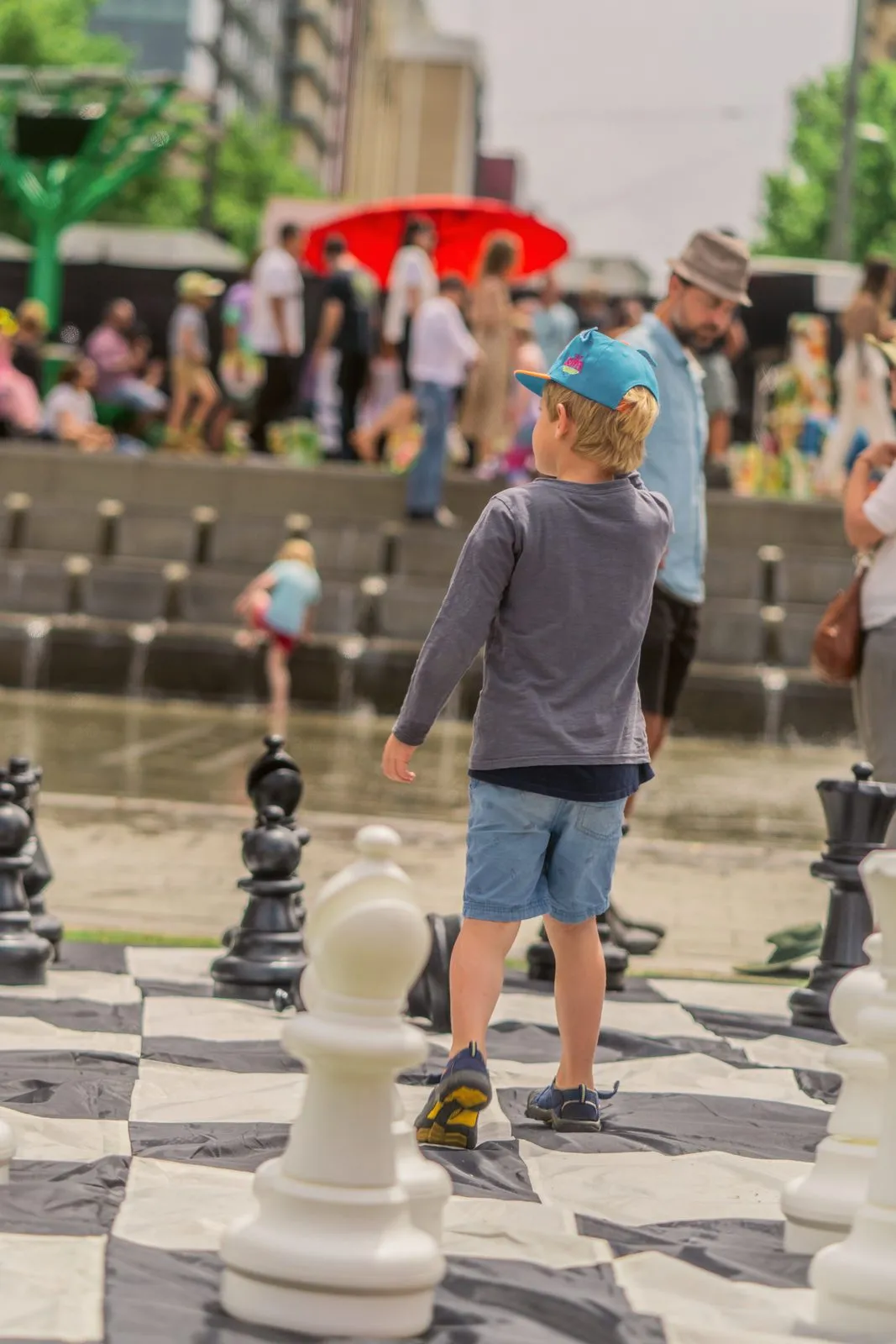 A small boy in a blue cap playing giant chess in a city square at a festival, Adelaide