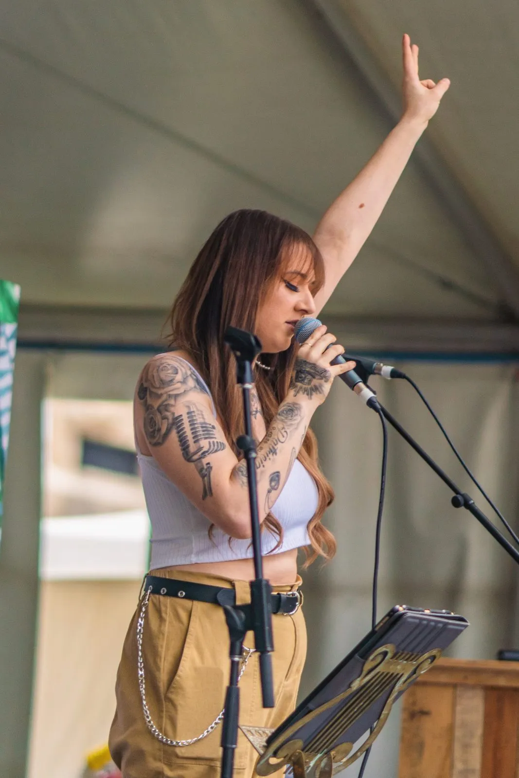 A tattooed singer at the microphone with her fist raised, on a festival stage