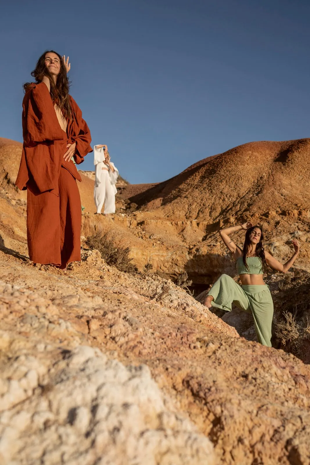 A model in a rust linen set on a red ridge, two others in cream and sage below her, Nomadica, Australia