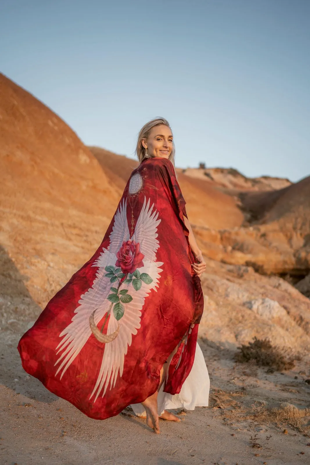 A model in a red winged kimono with a rose print, spread like wings against red cliffs, Nomadica