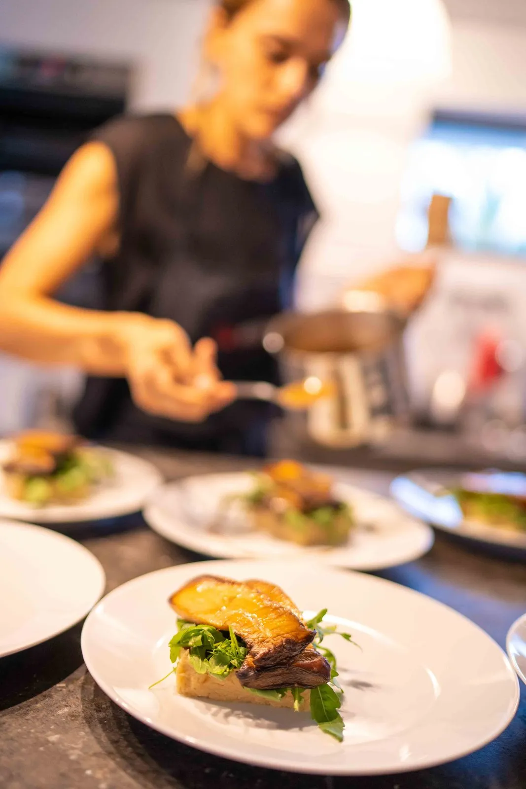A chef plating a row of dishes in a restaurant kitchen, one plate sharp in the foreground