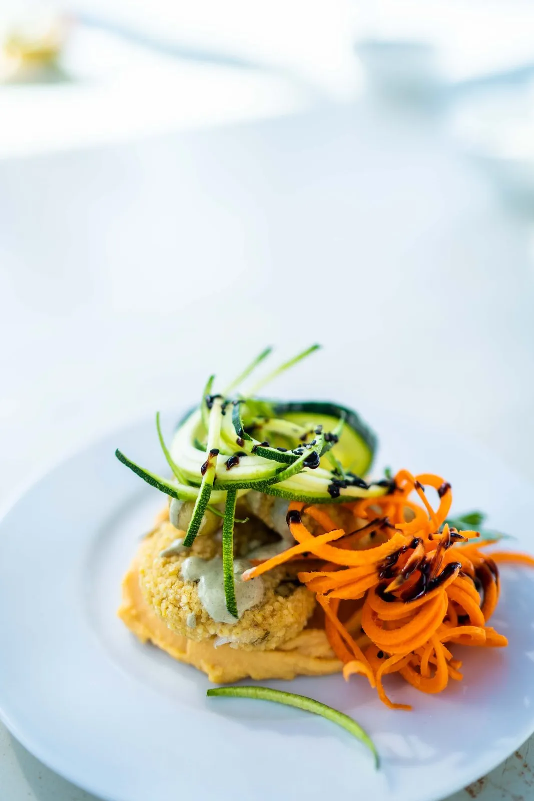 A plate of hummus topped with spiralised carrot, cucumber and seeds, in soft window light