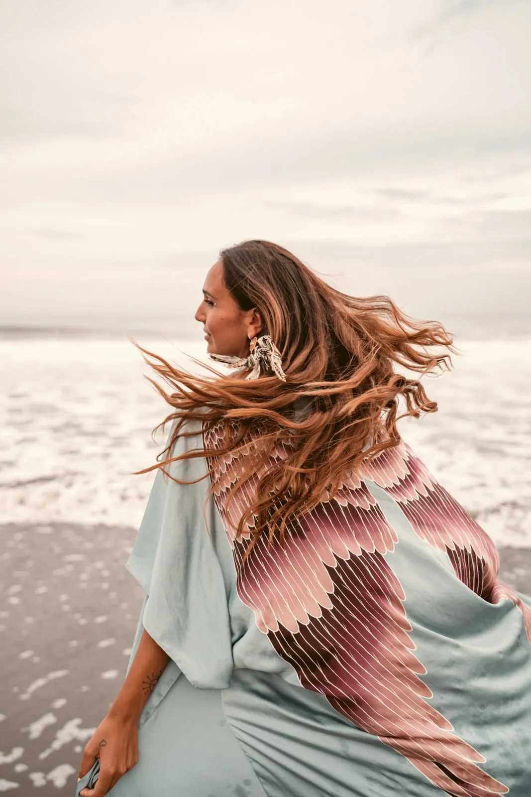 A woman in a pale blue winged kimono turning on the beach, her hair flying, Warriors of the Divine