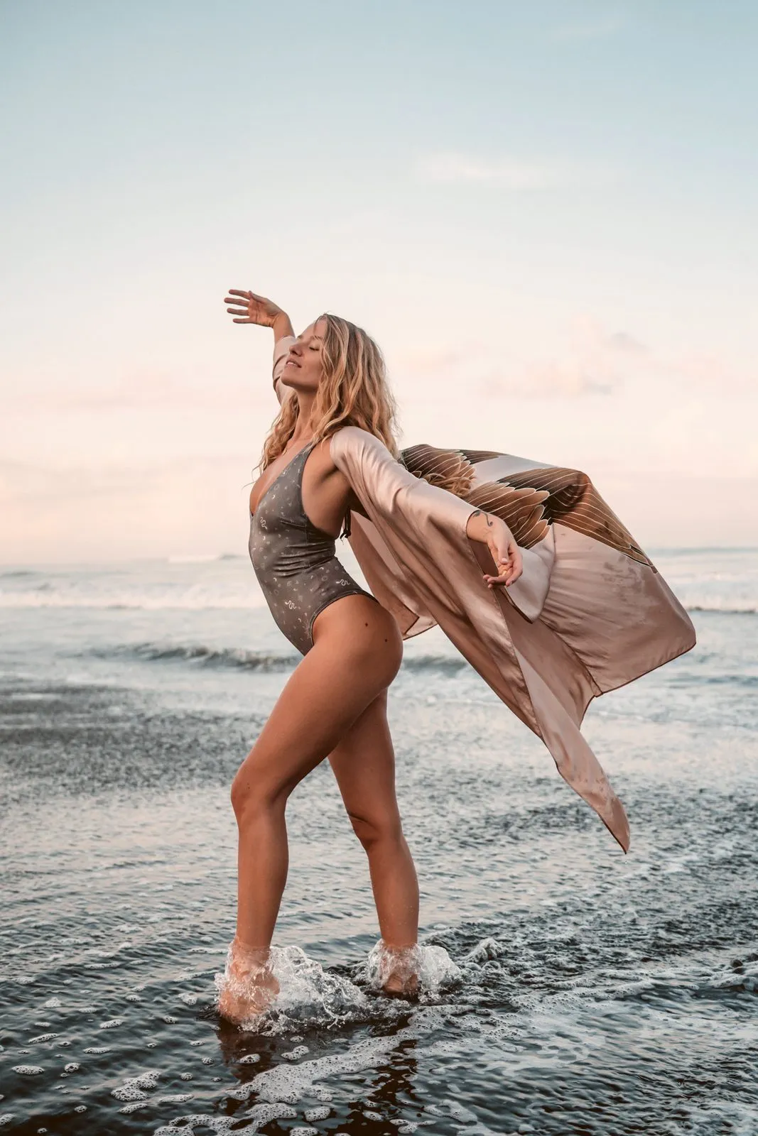 A woman in a sheer kimono dancing in the shallows at sunset, one arm raised, Warriors of the Divine