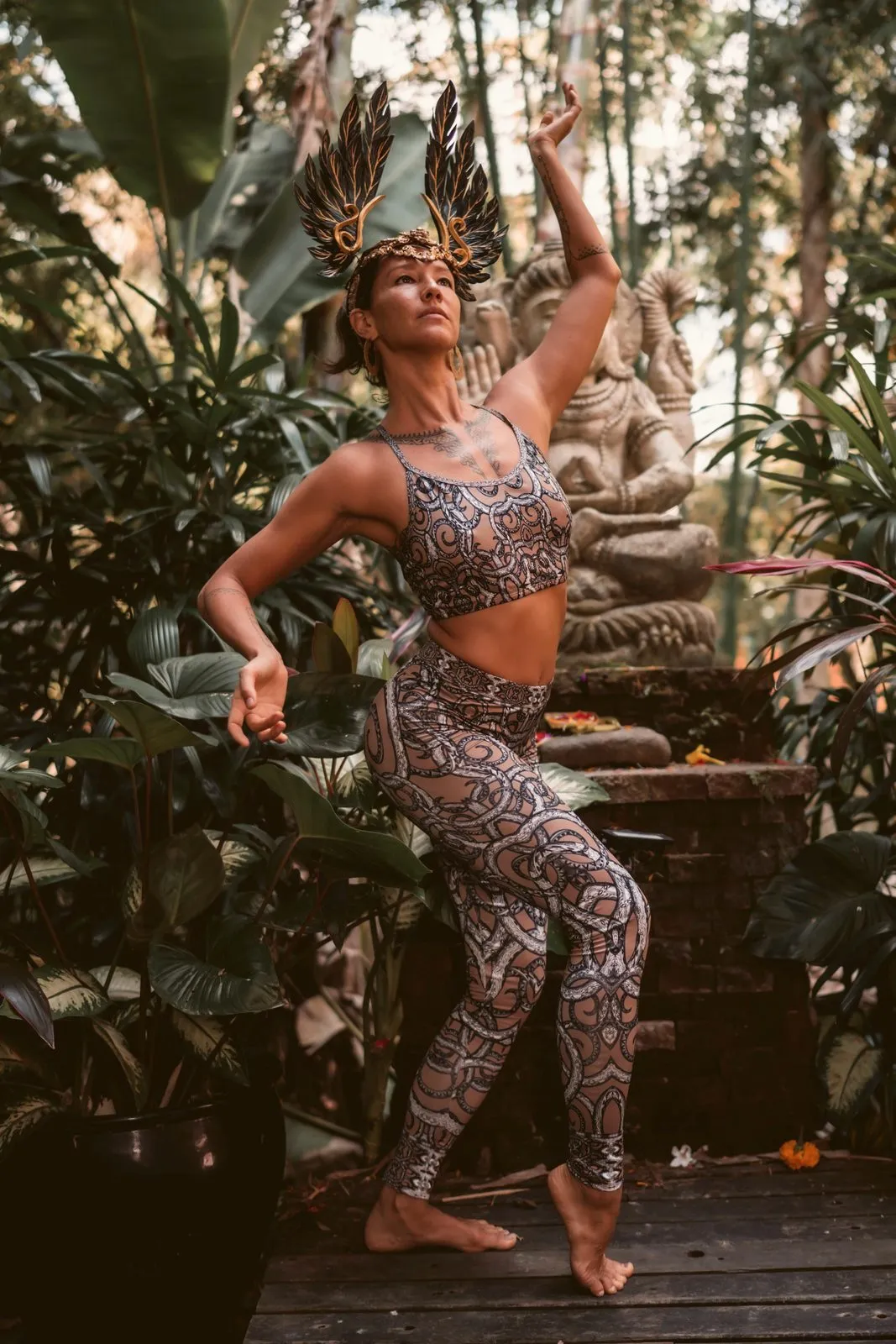 A woman in a feathered headdress and patterned Miramaya activewear dancing in a jungle garden