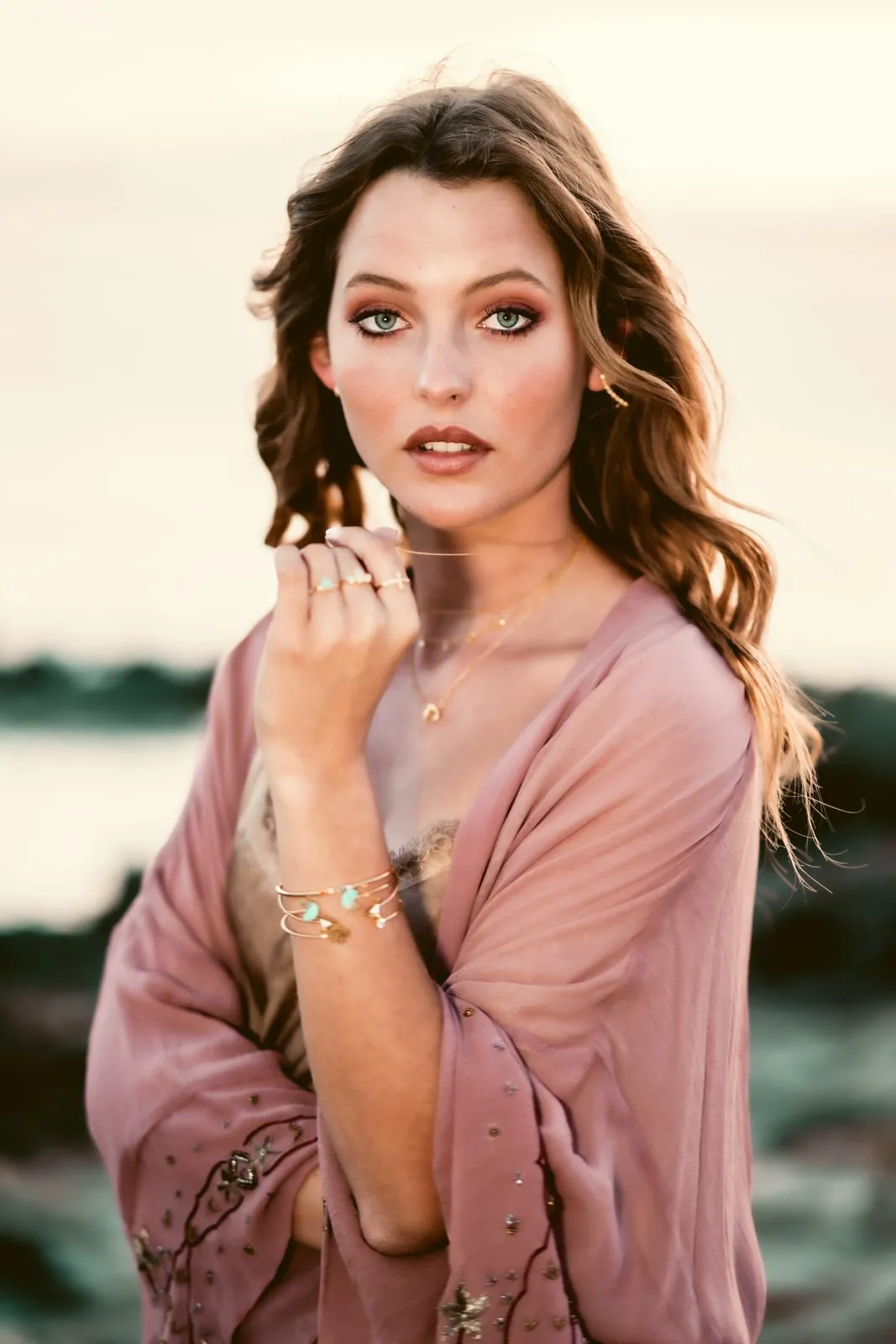 A model in a dusty pink kimono with gold jewellery on the rocks by the sea, Dreamers Ibiza
