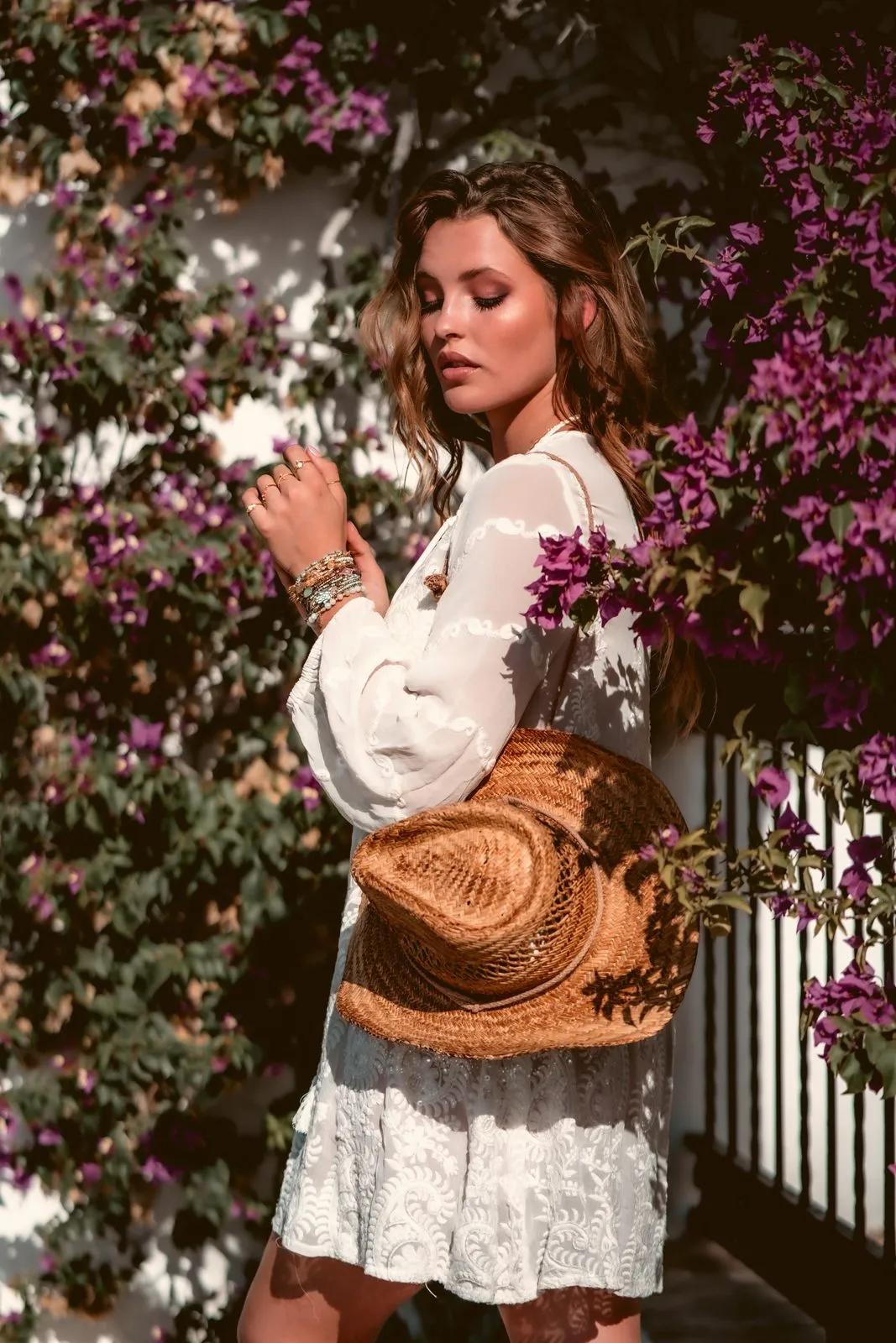 A model in a white dress with a straw hat beneath purple bougainvillea, Dreamers Ibiza