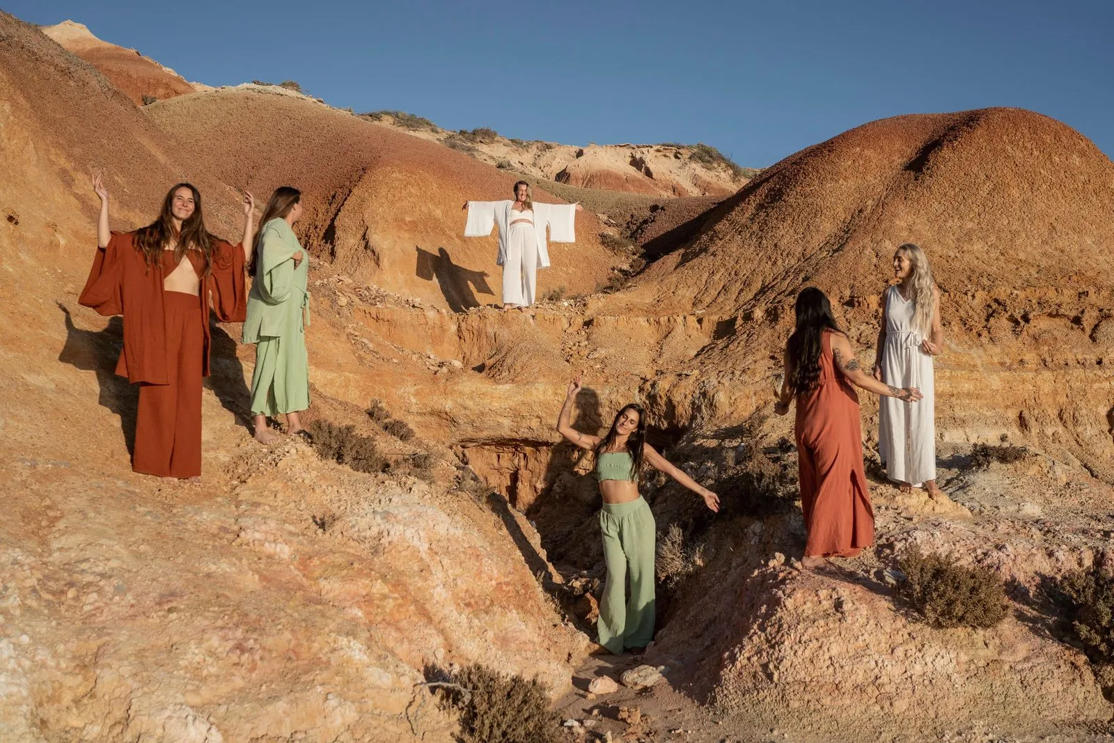 Five models in rust, sage and cream linen posed across red earth cliffs by the sea, a Nomadica campaign in Australia