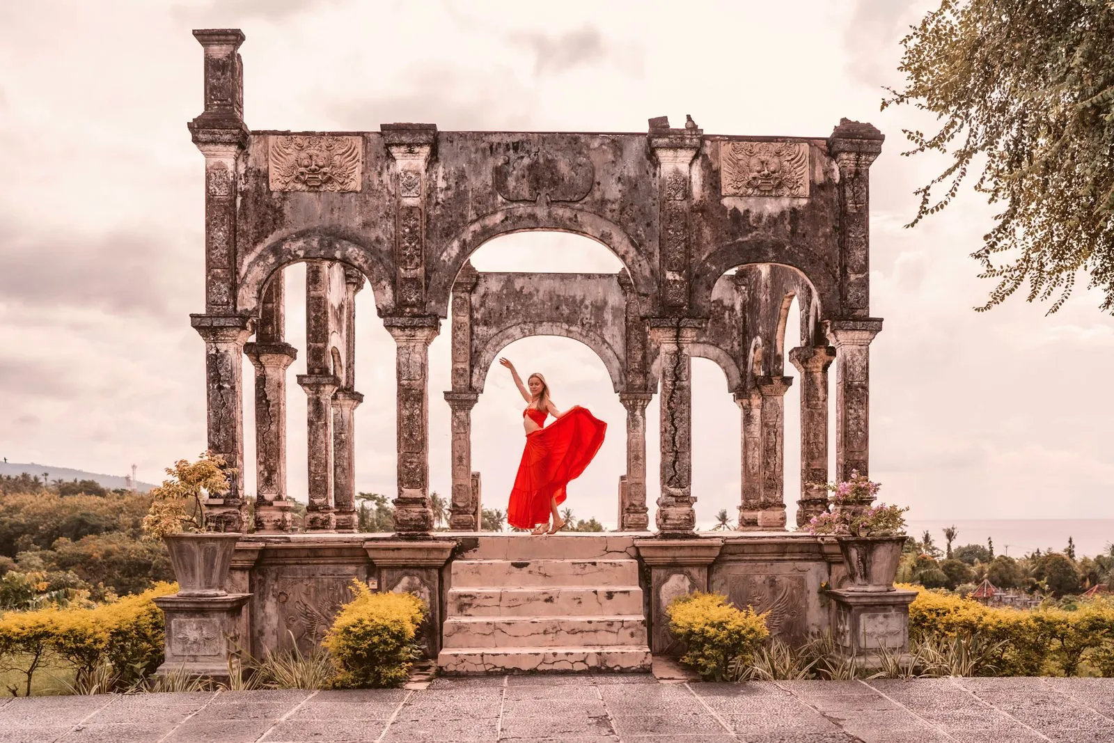 A woman in a red dress dancing beneath a ruined stone archway in Bali
