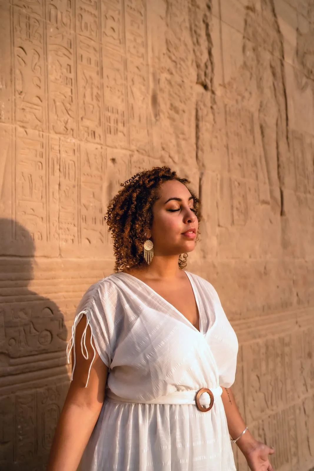 A woman in white against a wall of carved hieroglyphs in the golden light of a temple in Egypt
