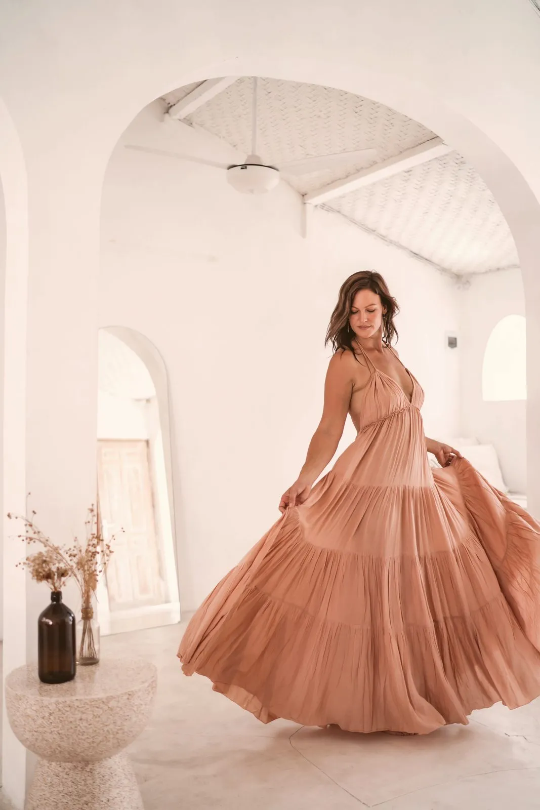 A woman in a long blush dress turning so the skirt flares, in a white room with arched doorways