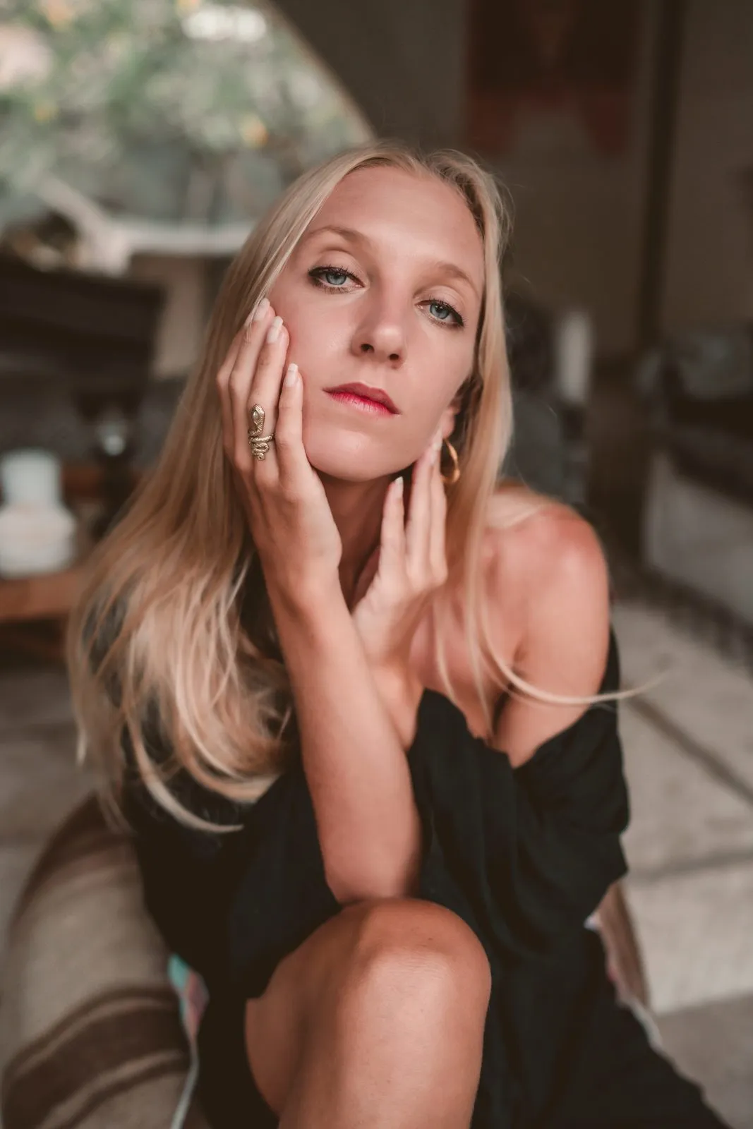 A woman in a black off-the-shoulder top looking to camera with her hand at her cheek