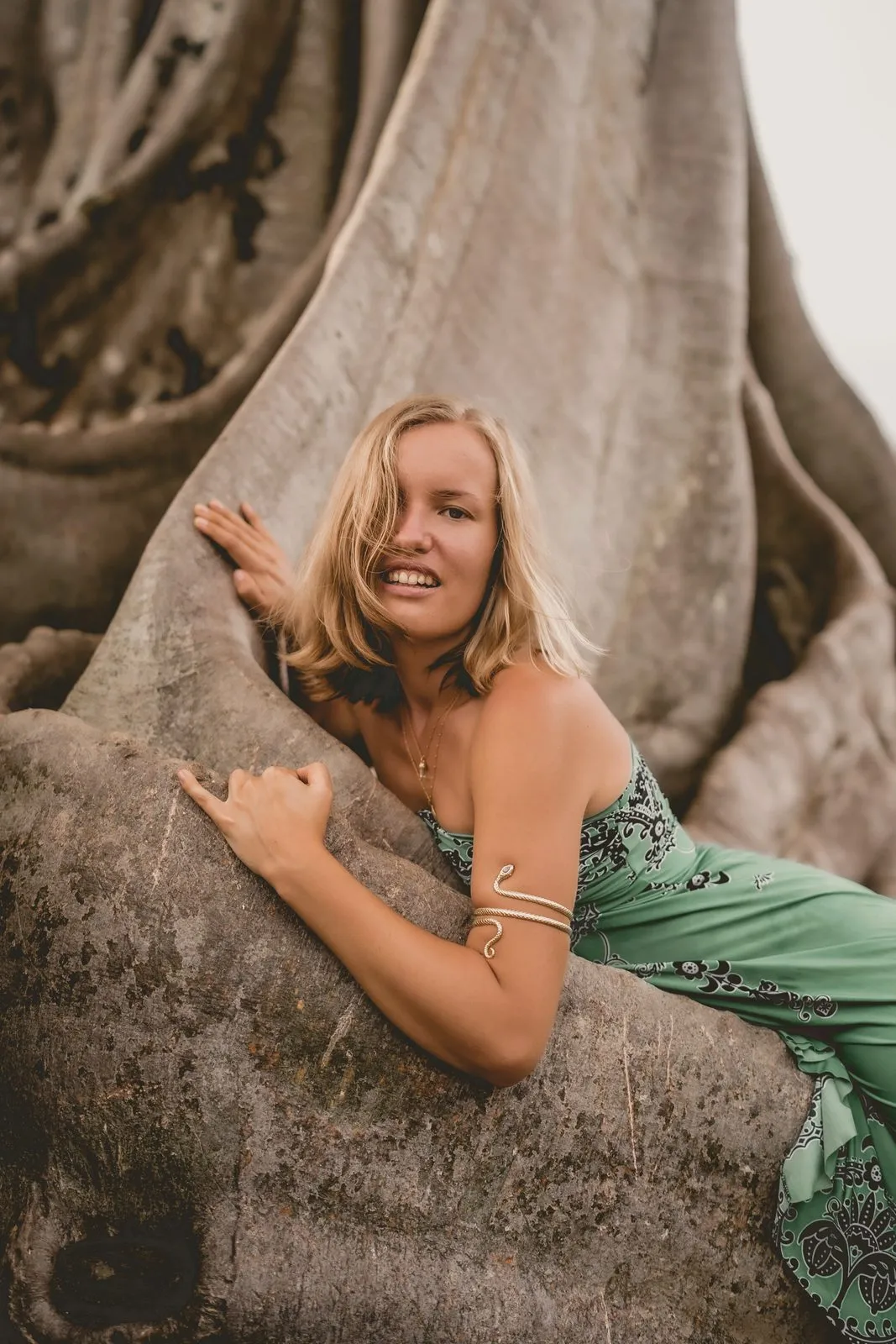 A woman in green climbing the buttress roots of a giant banyan tree, laughing