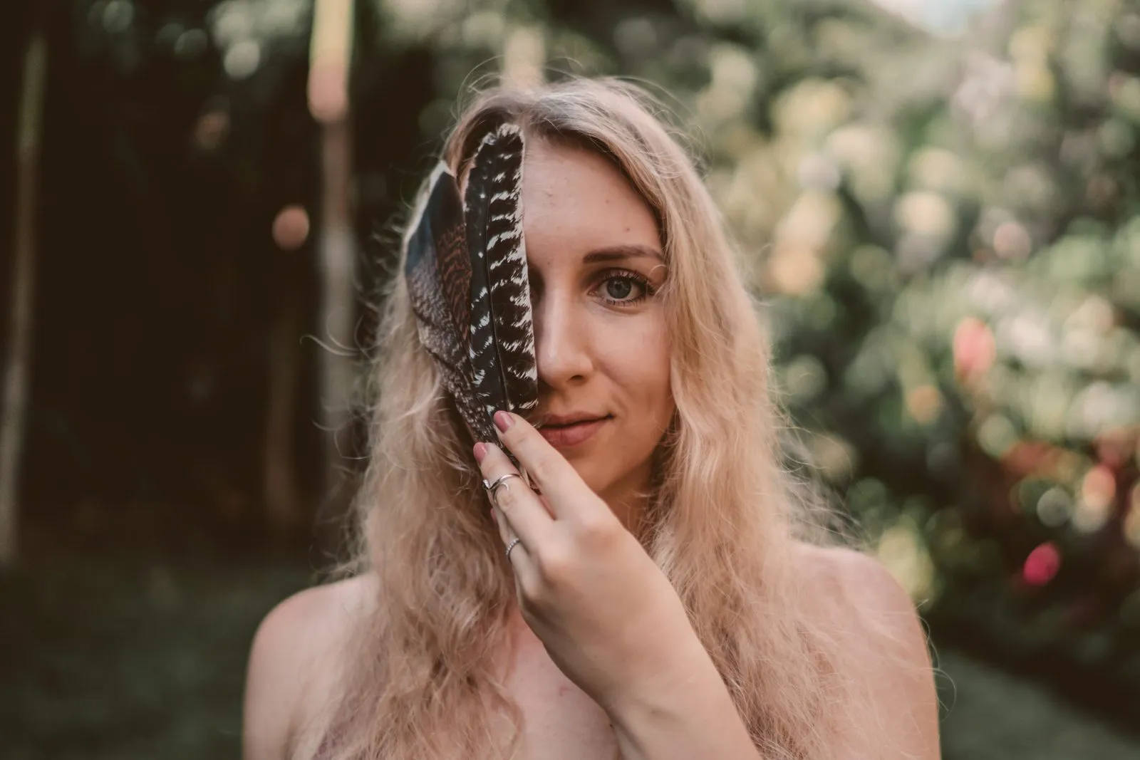 A close portrait of a woman holding a striped feather over one eye