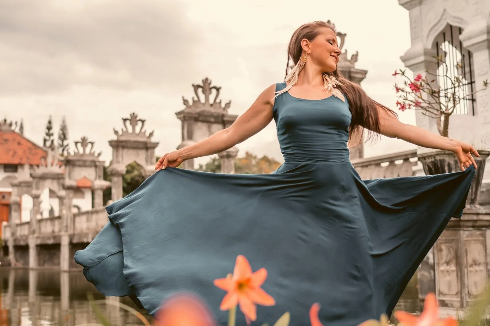 A woman in a teal dress spreading her skirt like wings at the water palace gardens in Bali
