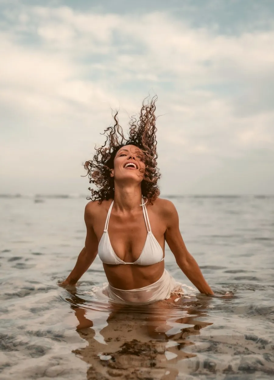 A woman in a white bikini rising out of the sea, flicking her wet hair back