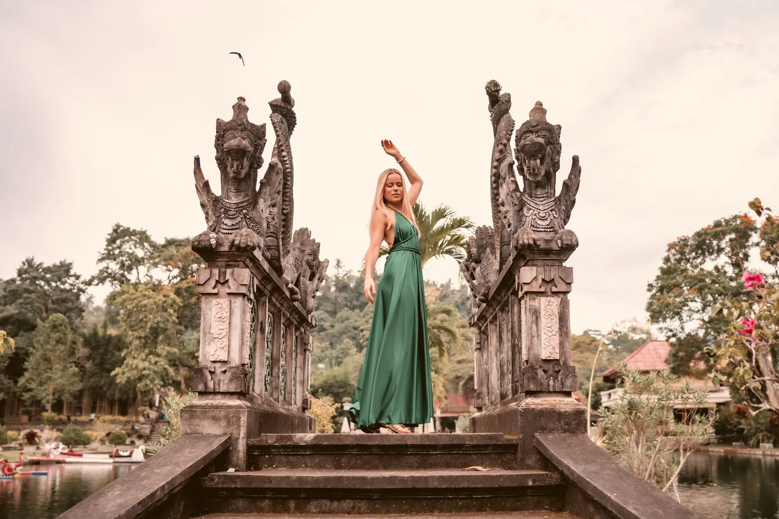 A woman in a green dress, one arm raised, between the carved stone pillars of the Gates of Heaven at Lempuyang temple, Bali