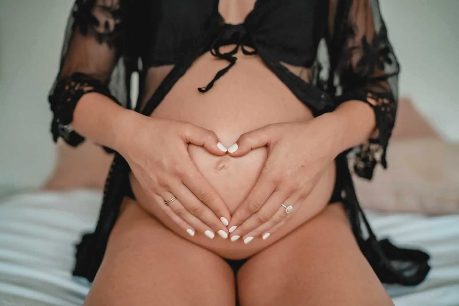 Hands forming a heart over a bare pregnant belly, a black lace robe open around it