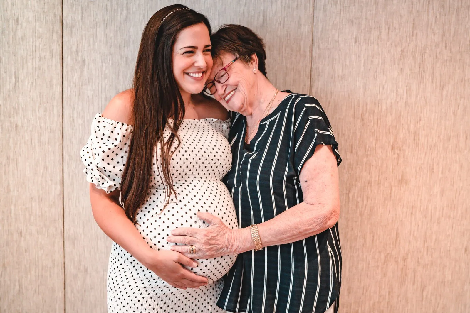 A pregnant woman and an older woman laughing cheek to cheek at a baby shower, hands on the belly