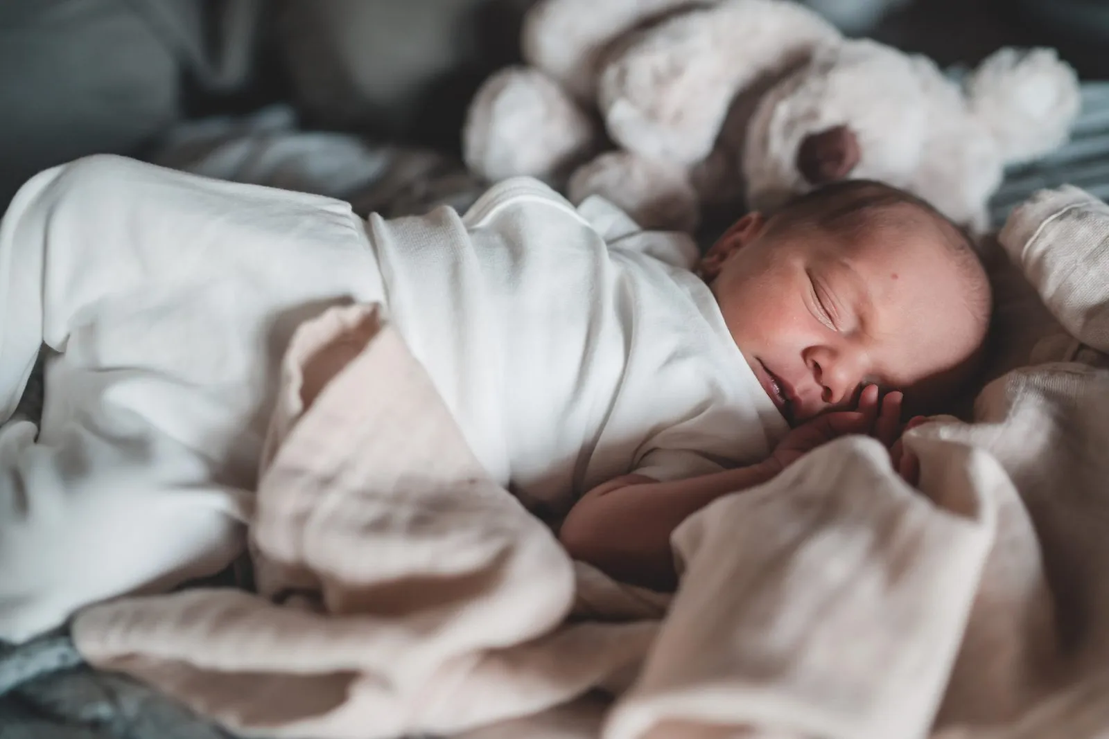 A newborn swaddled in cream muslin asleep among soft blankets