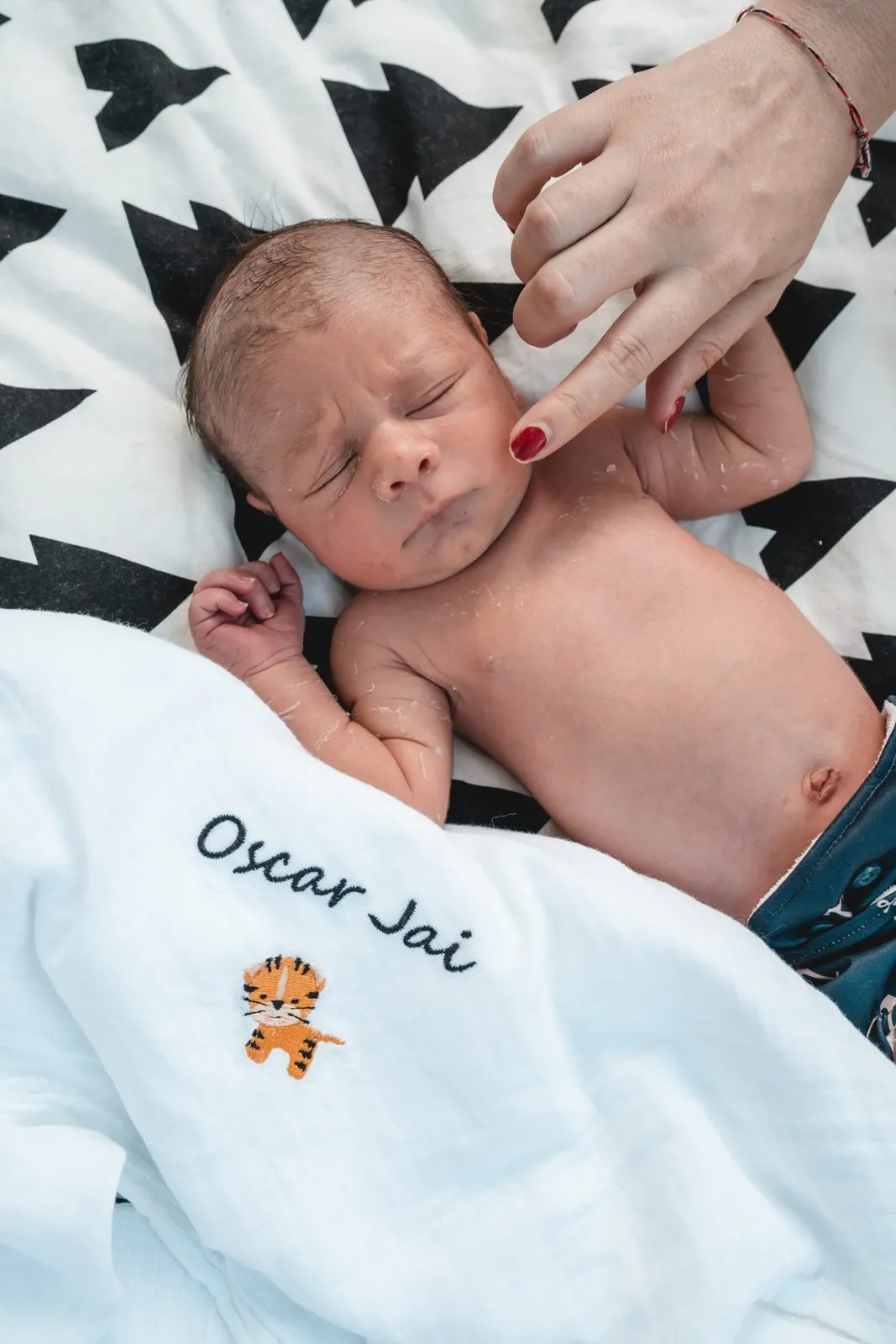 A newborn boy on a patterned blanket, a mother's hand resting on his cheek