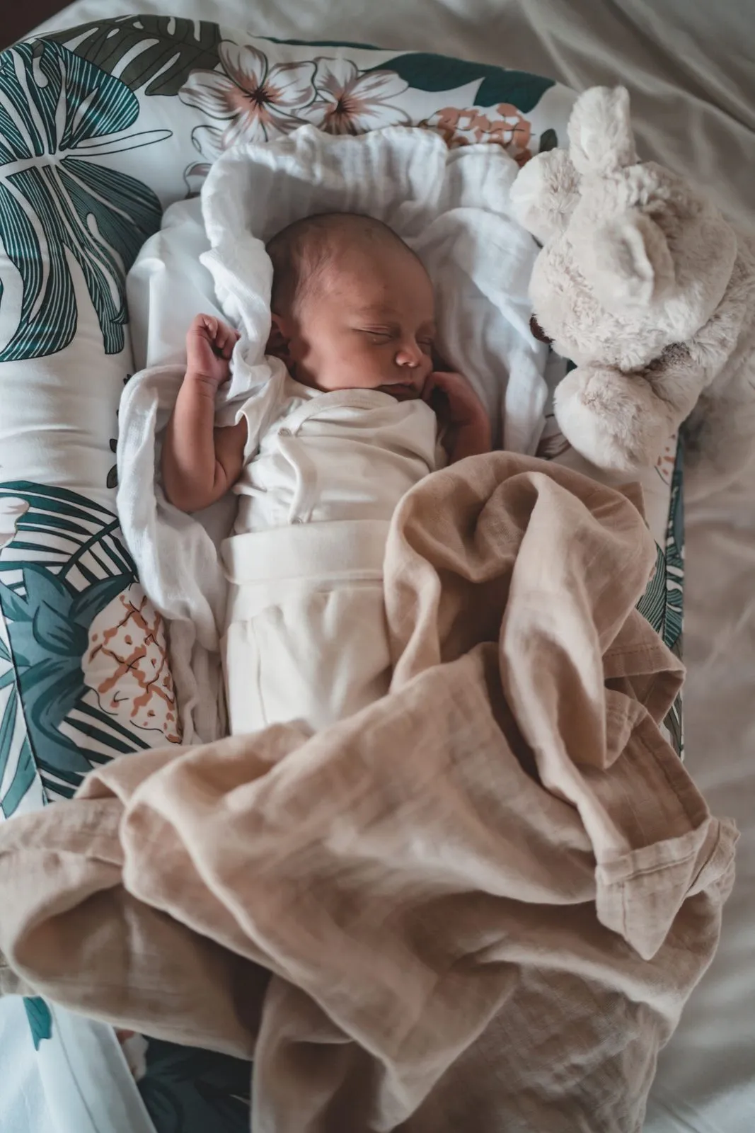 A newborn lying in a leaf-print bassinet with a knitted bunny beside her