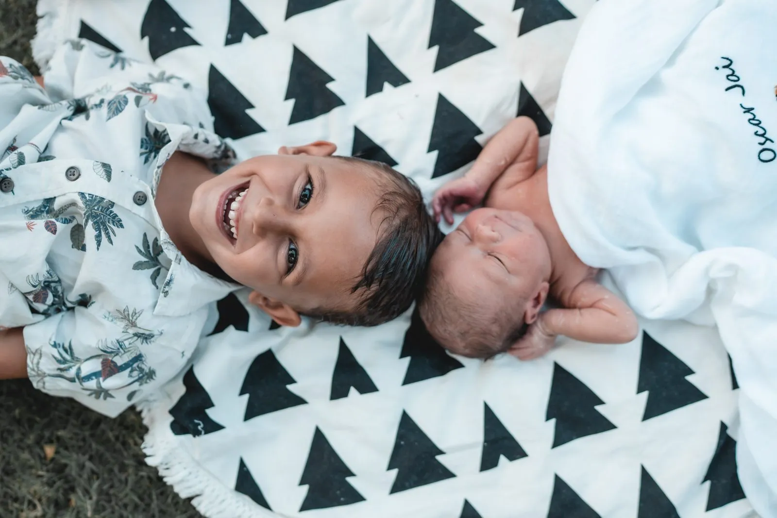 A laughing boy lying beside his newborn brother on a black and white blanket