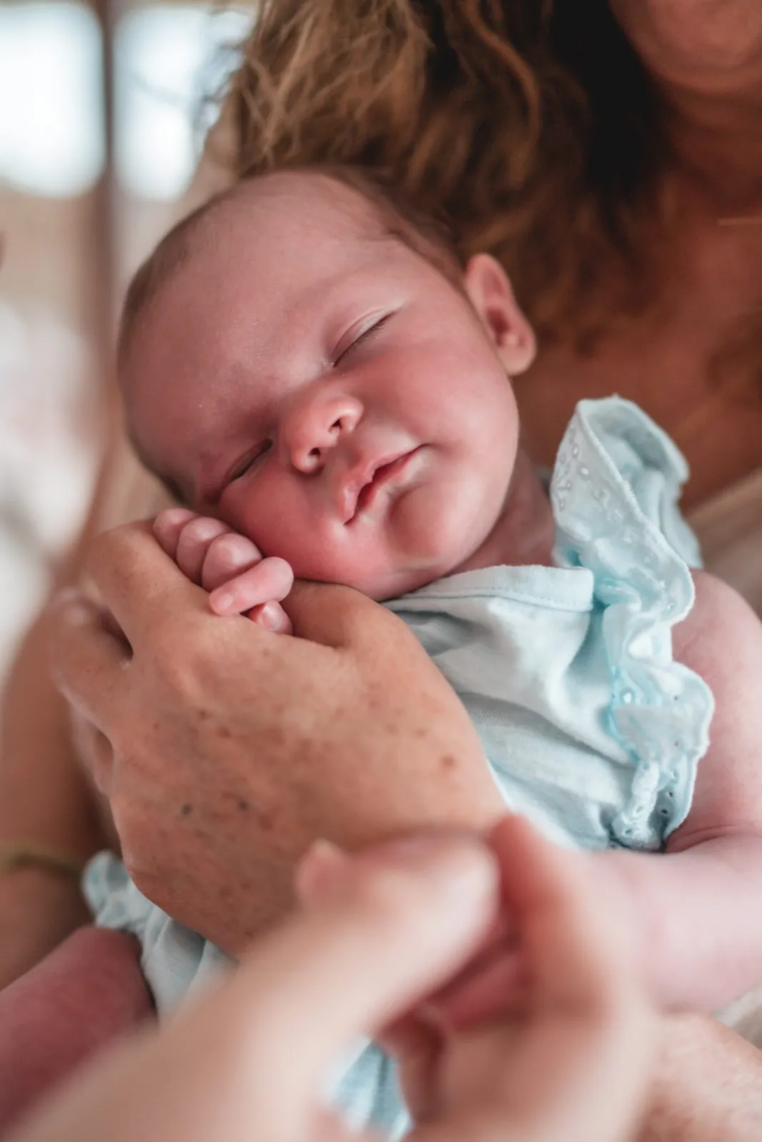 A newborn in a pale blue frill held up against her mother's shoulder, eyes closed