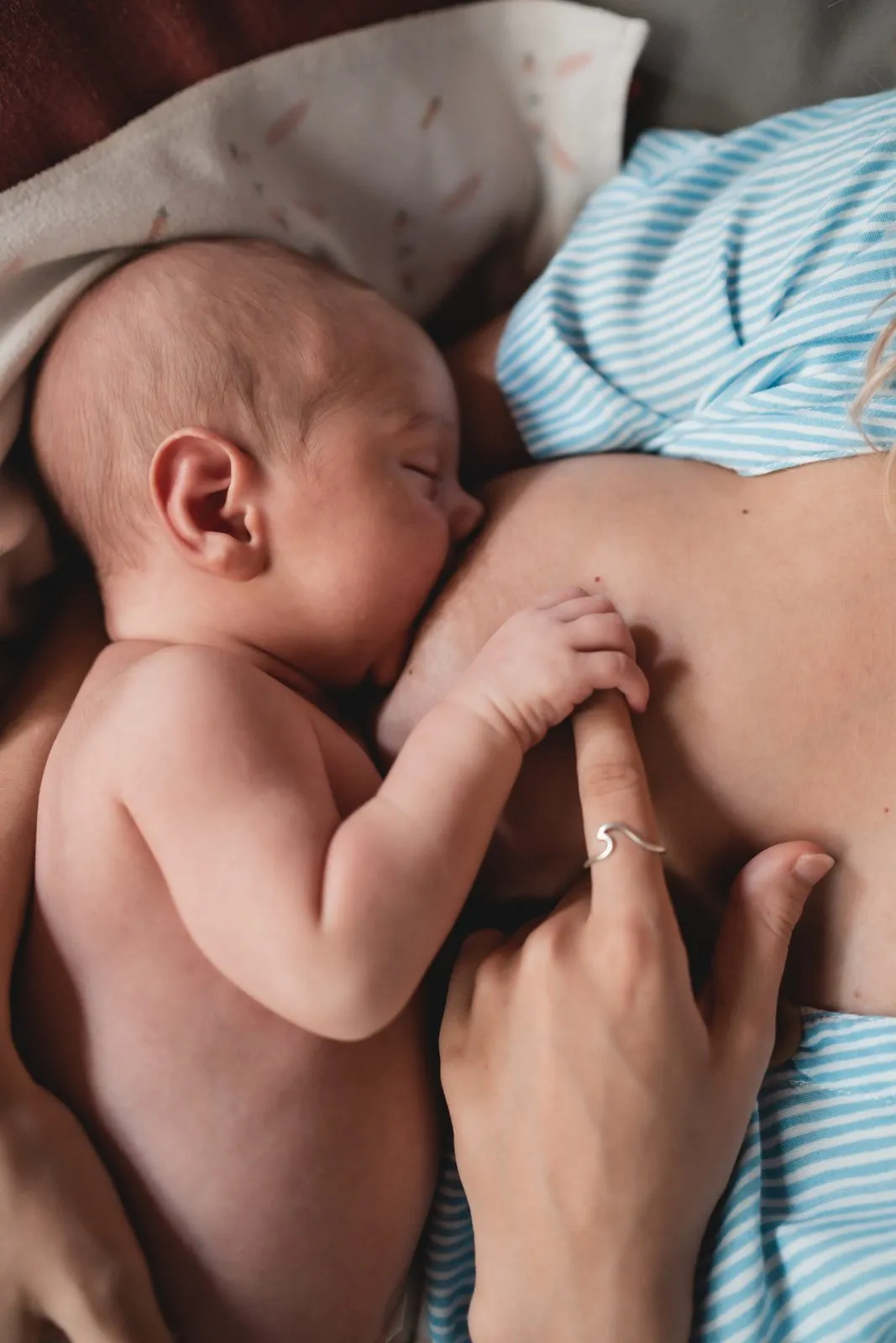 A newborn feeding at the breast, one small hand resting on the skin