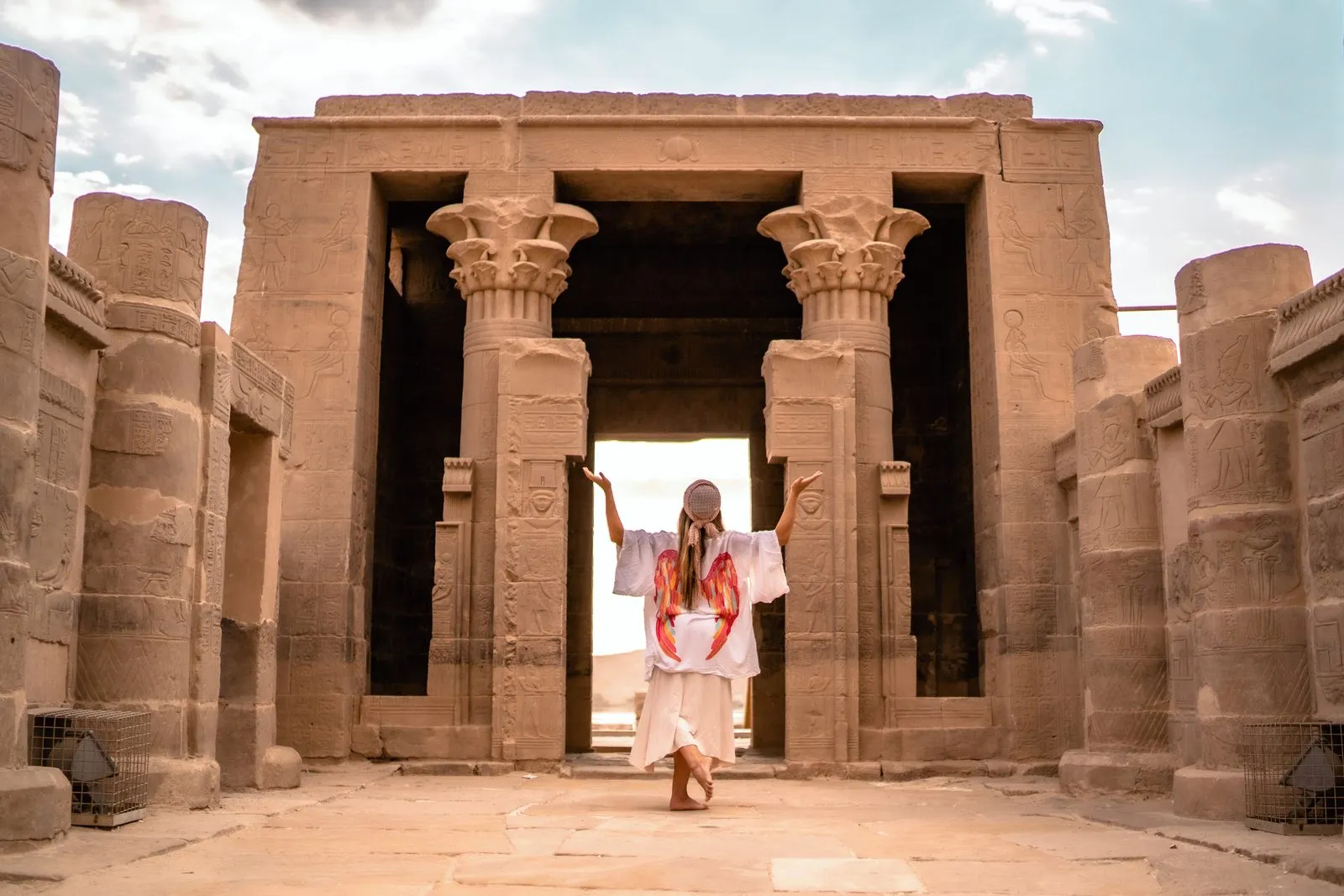 A woman in white standing in the gateway of the temple of Isis at Philae, arms raised, Egypt