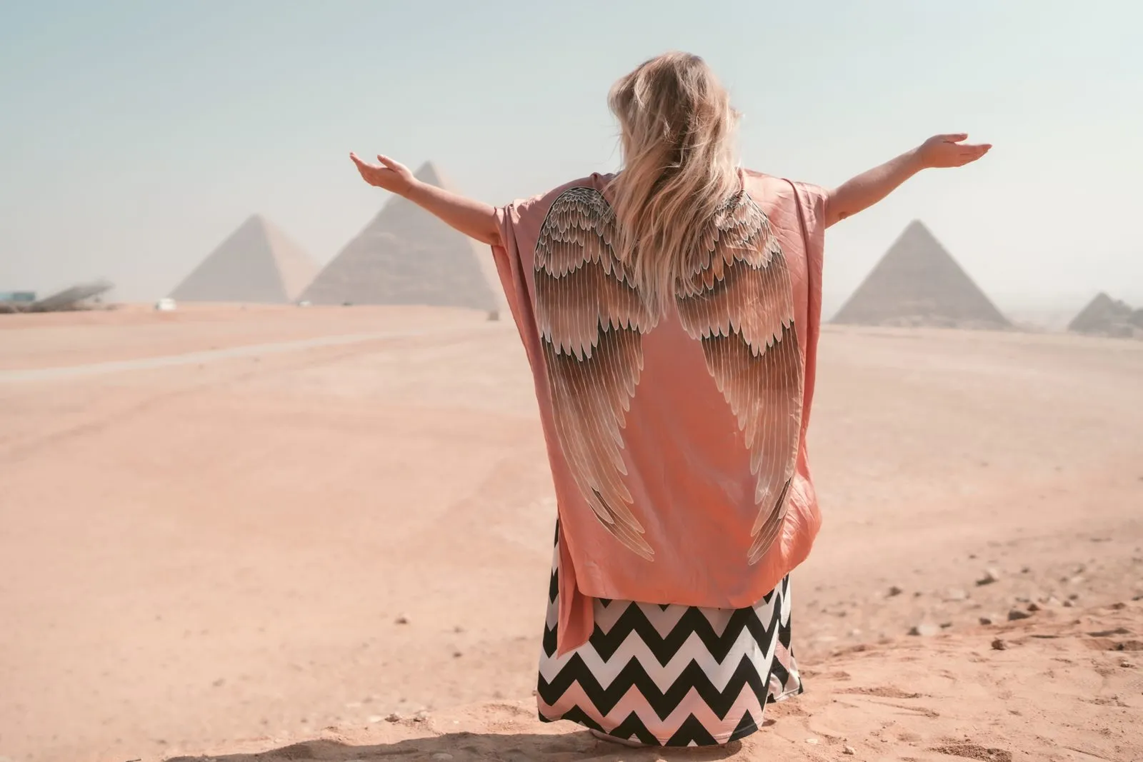 A woman in a winged kimono with her arms open to the pyramids of Giza, Egypt
