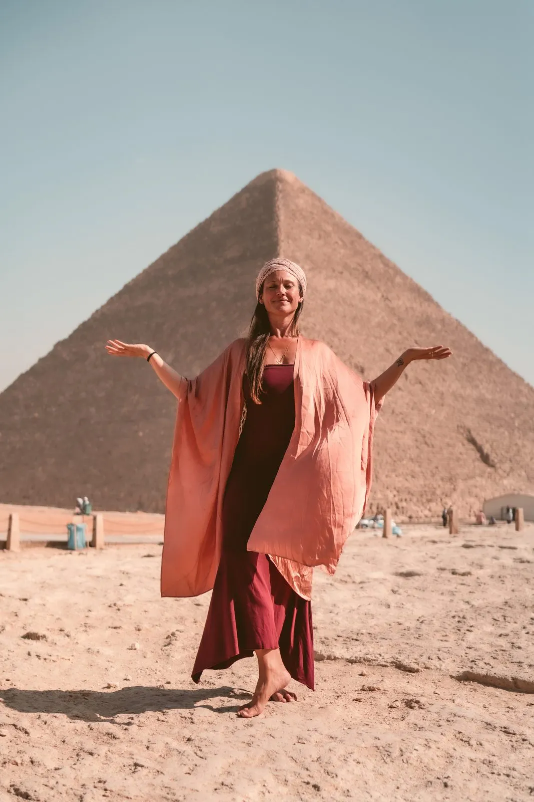 A woman in a coral kimono with her arms open before the Great Pyramid, Giza