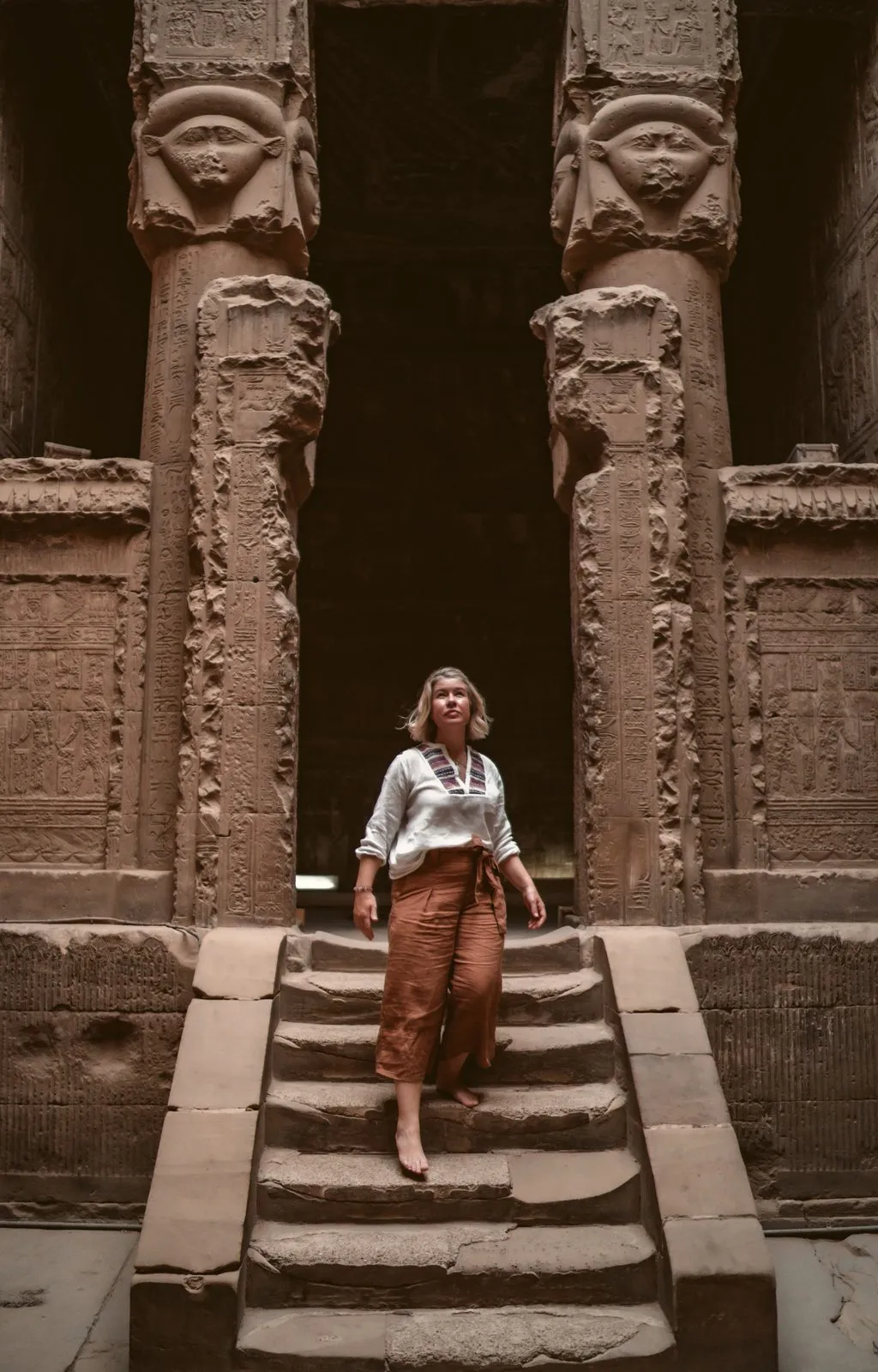 A woman on the steps between the Hathor columns of a temple gateway in Egypt