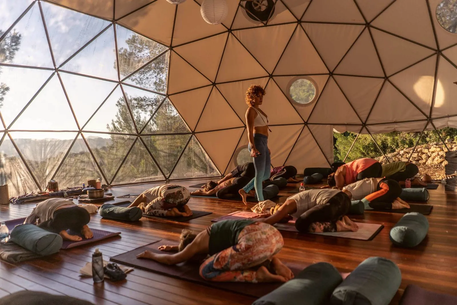 A yoga class resting in child's pose inside a geodesic dome on retreat in Ibiza, the teacher walking between them