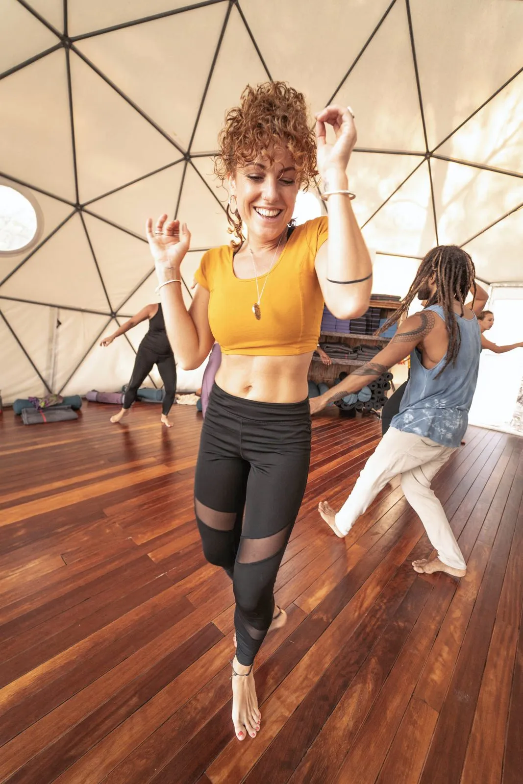 A woman in a yellow top dancing barefoot on a wooden floor inside a dome, others moving behind her, Ibiza