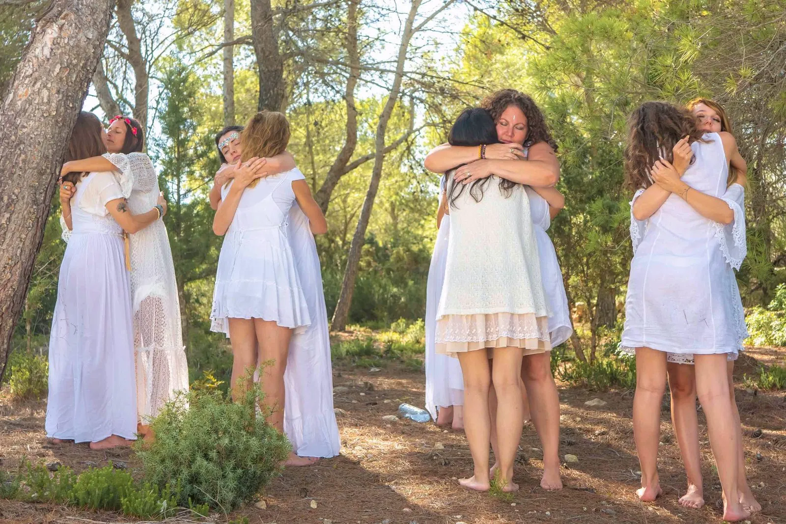Women in white embracing in pairs among pine trees on a retreat in Ibiza