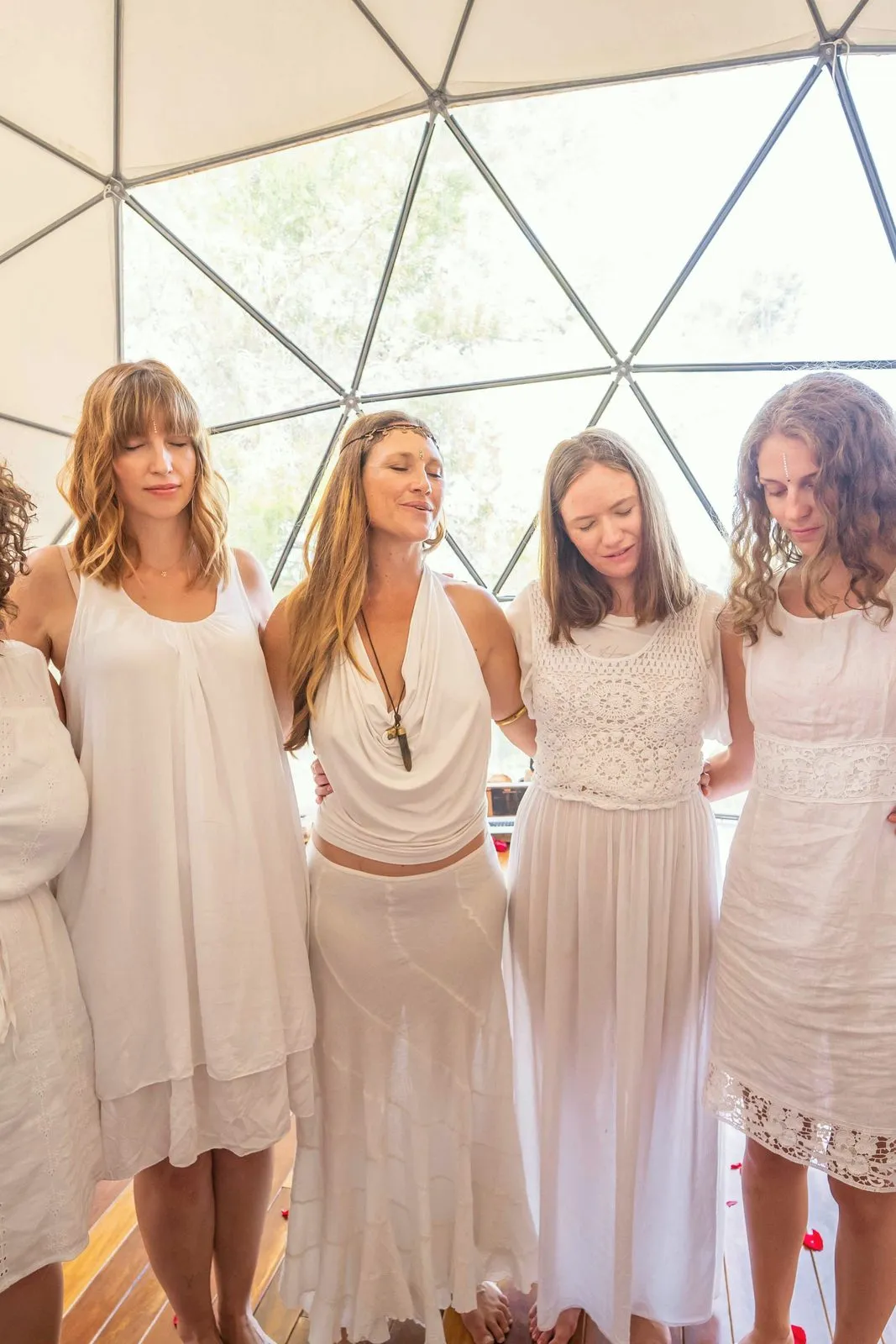 A circle of women in white with their heads bowed together inside a geodesic dome, Ibiza