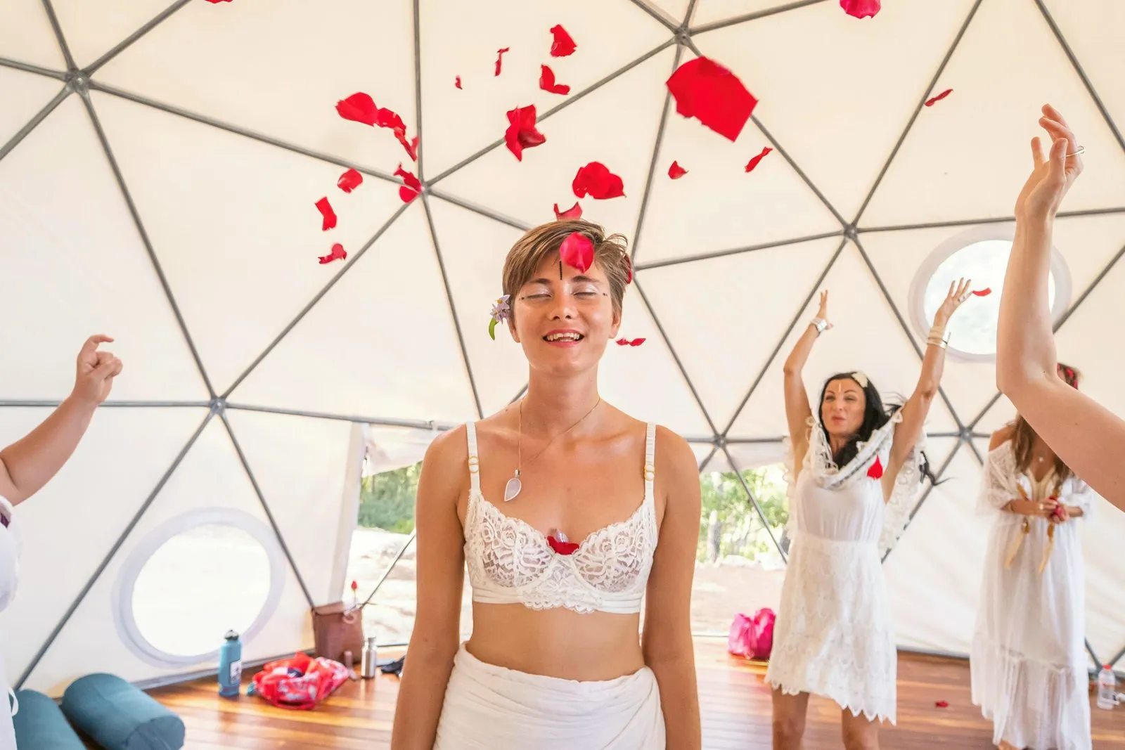 Women in white throwing red petals into the air inside a dome, laughing, Ibiza
