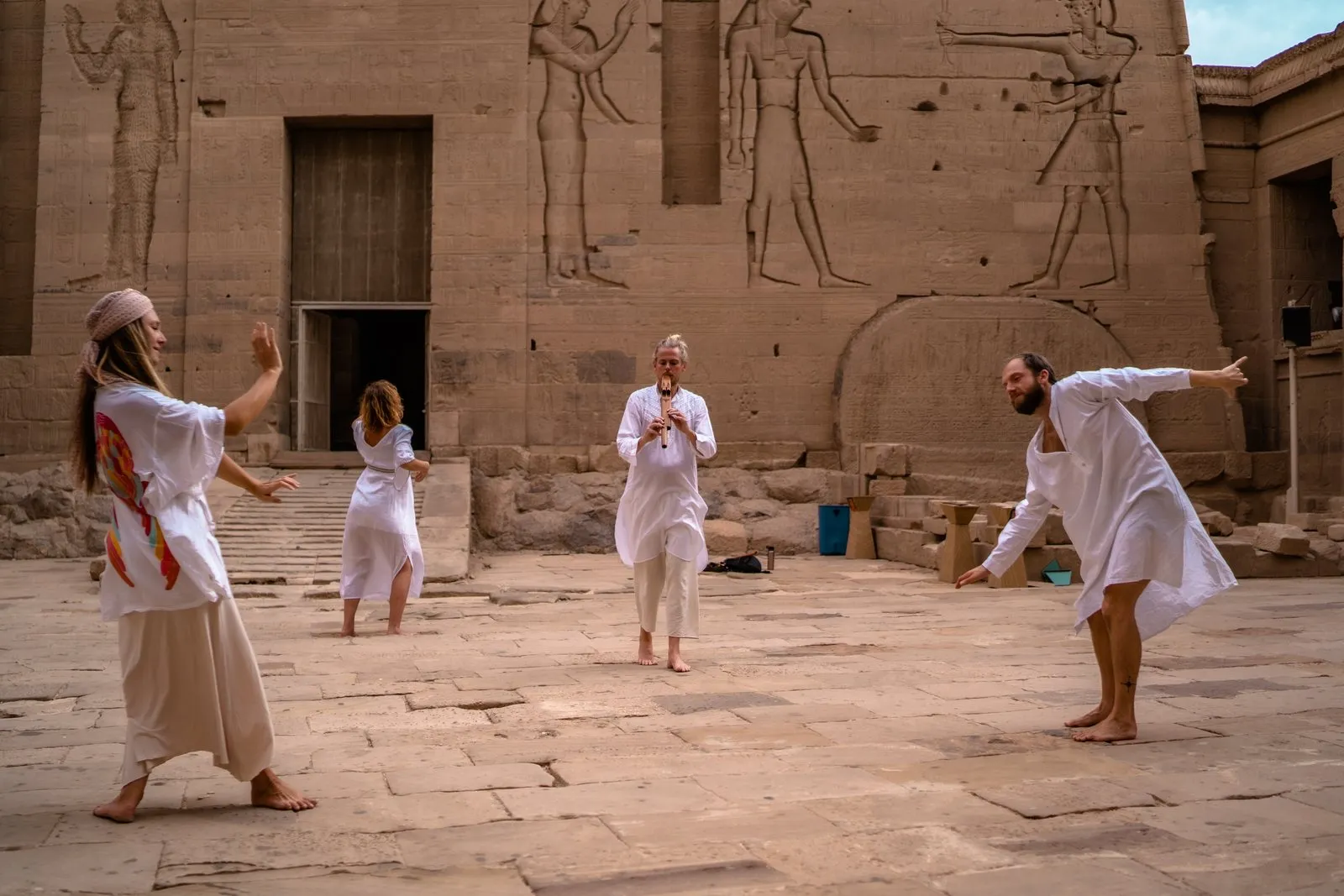 Women in white moving through a temple courtyard in Egypt, carved reliefs on the walls behind them