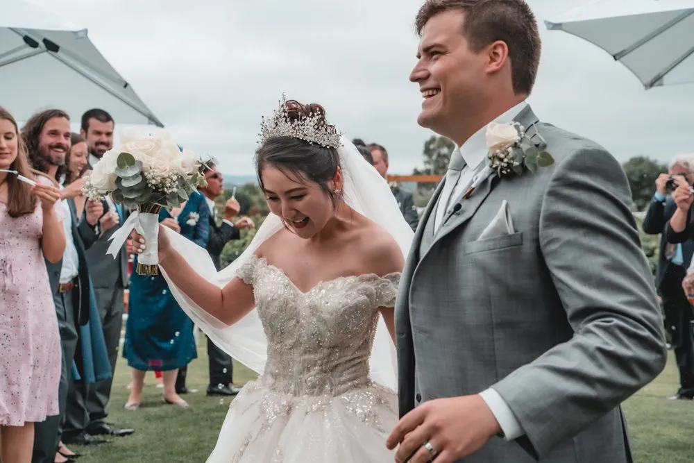 A bride and groom laughing as guests throw petals over them after the ceremony