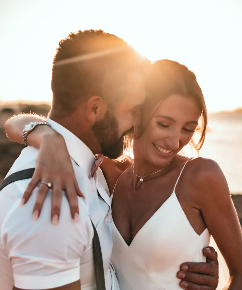 Wedding photography, a bride laughing in her husband's arms as the sun goes down behind them